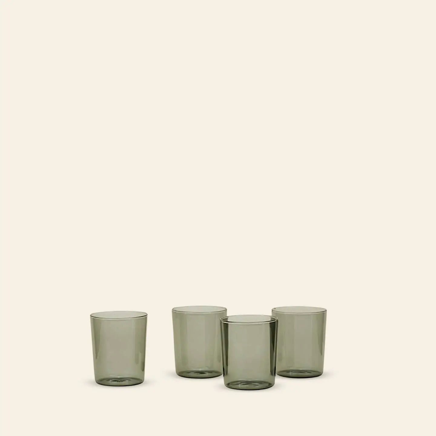 A set of four translucent grey Hawkins New York Essential Glassware (medium size) is arranged in a row on a plain light beige background, with two glasses in front and two slightly behind, highlighting their premium quality.