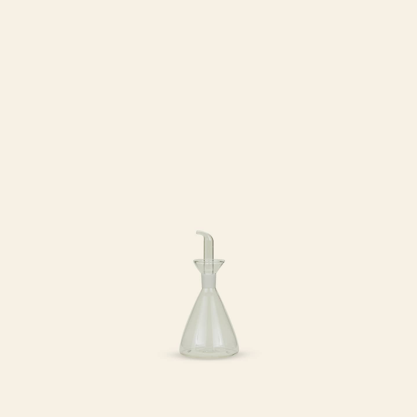 The Hawkins New York Essential Kitchen Bottle, Medium, is a clear, modern bottle with a narrow neck, funnel-shaped top, and precision drizzle spout. It sits centered on a plain light beige background for a minimalistic look.