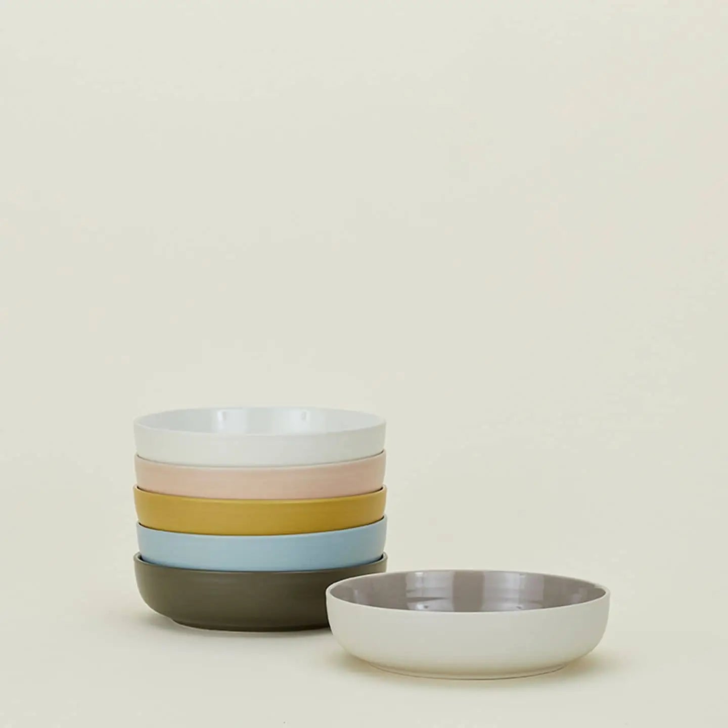 A set of four Hawkins New York Essential Low Bowls in pastel hues, with an additional matching bowl in front, adds a refined touch to your dining setting against a simple light background.