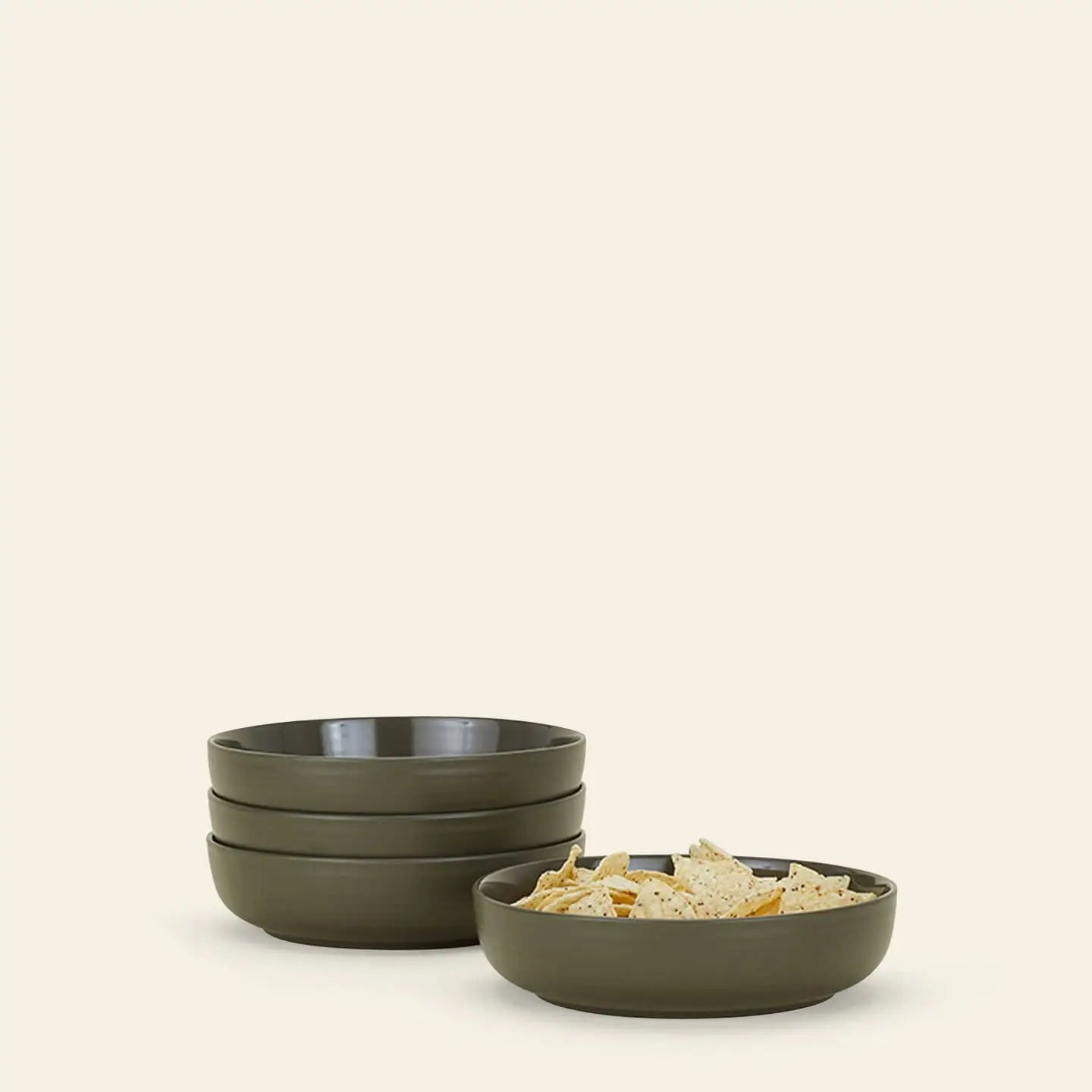 A set of four olive green Hawkins New York Essential Low Bowls is arranged beside a matching bowl filled with tortilla chips, all against a plain light beige background, adding style to any dining setup.