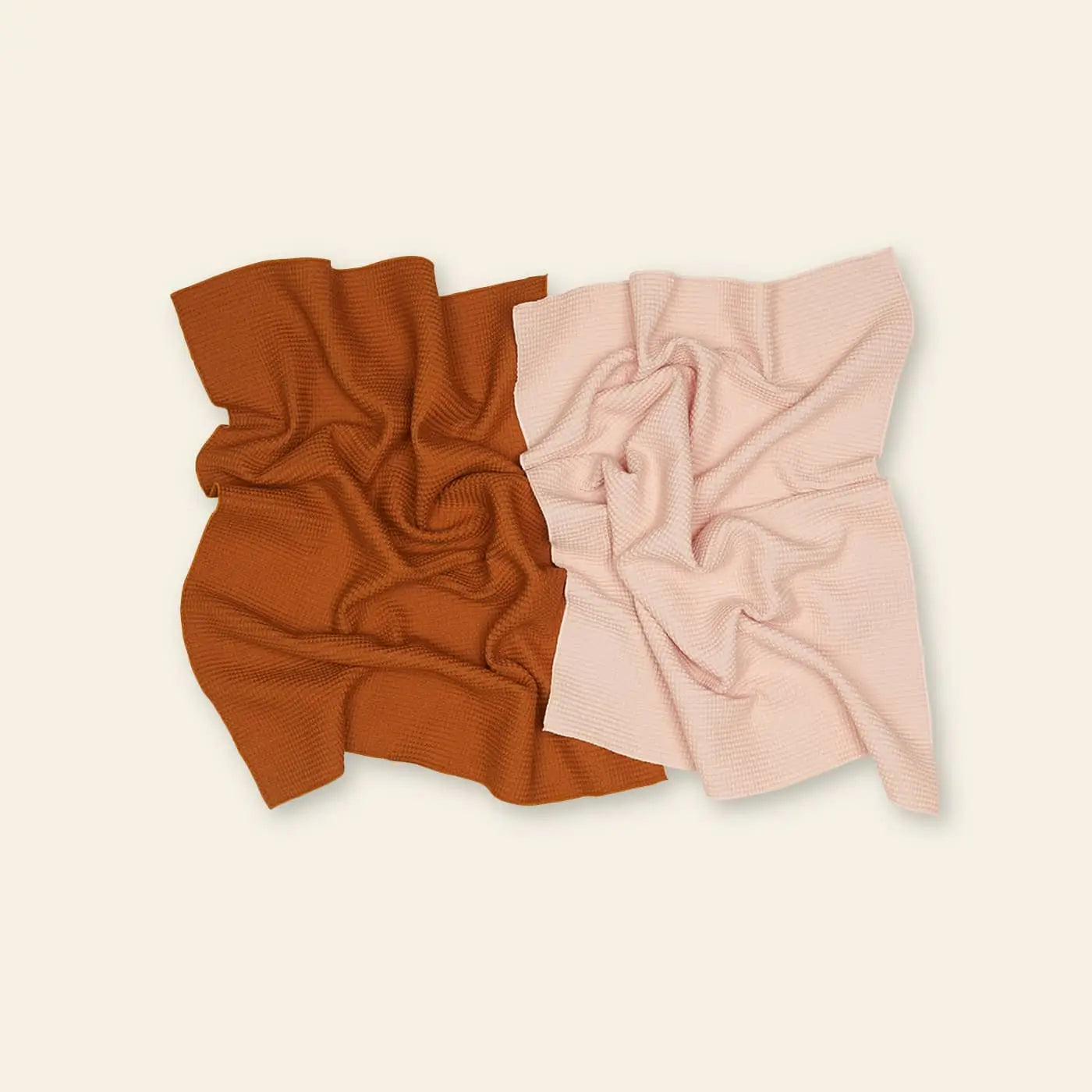 Two rectangular Hawkins New York Essential Waffle Dish Towels—a rust orange and a pale pink—are displayed side by side on a plain, light beige background.