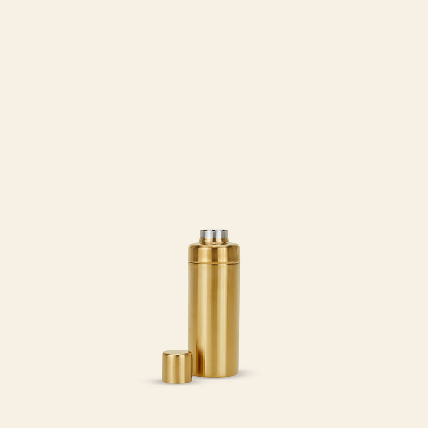 A metallic gold Hawkins New York Simple Cocktail Shaker by Hawkins New York stands upright with its lid beside it, reminiscent of a sleek thermos, against a plain beige background.