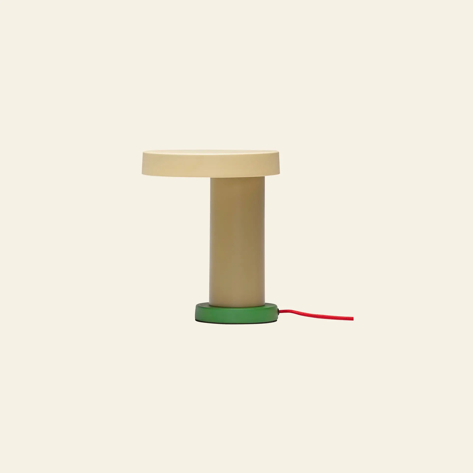 The Hübsch Magic Table Lamp by Hübsch is a minimalist beige lamp with a round flat top, cylindrical base, green bottom, yellow fabric cord, and dimmable touch control, shown against a plain light background.
