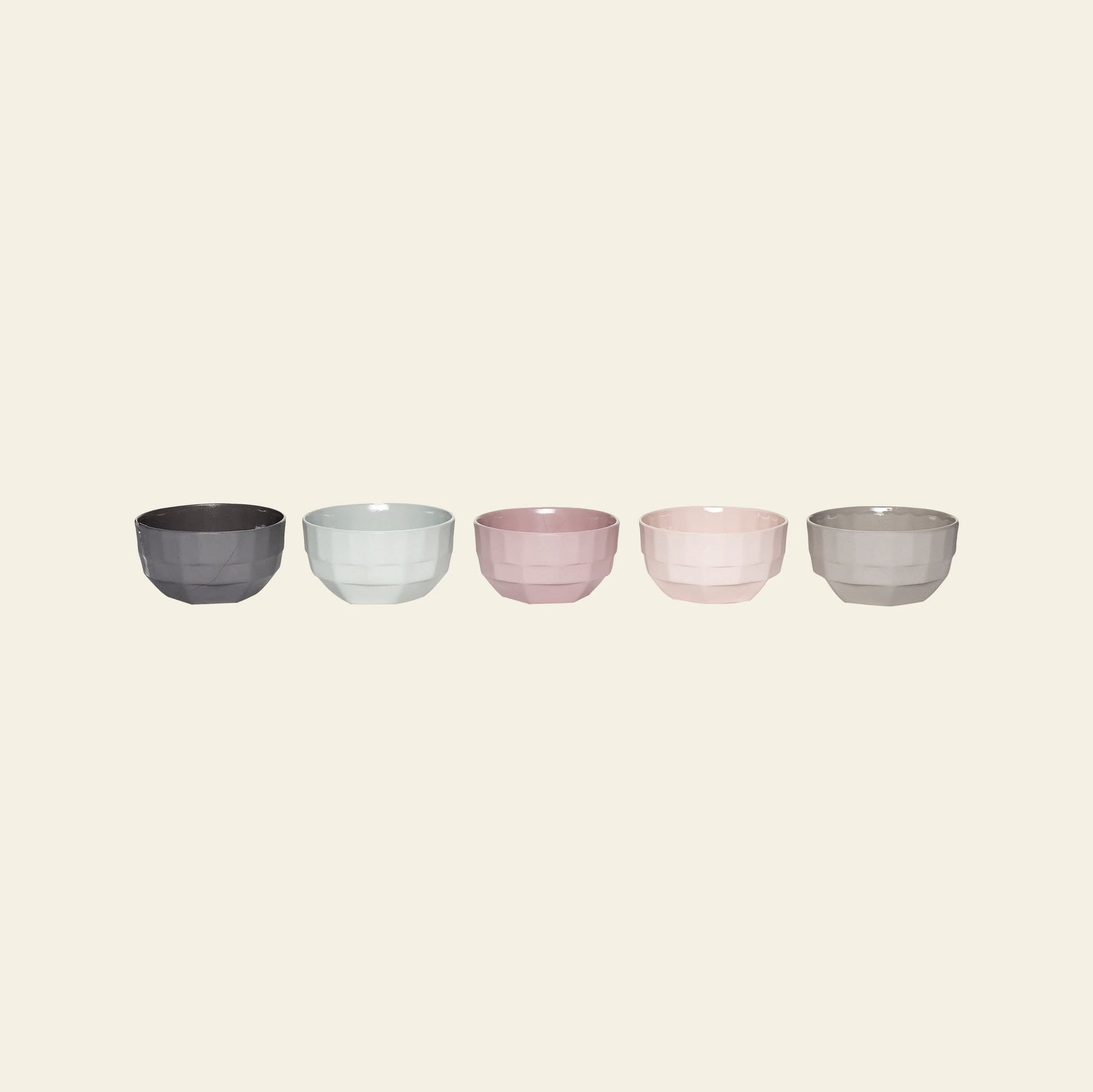 The Hübsch Select Bowls, Set of 5 by Hübsch features small, faceted porcelain bowls in dark gray, light blue, light pink, soft peach, and beige, arranged in a row on a plain light background.