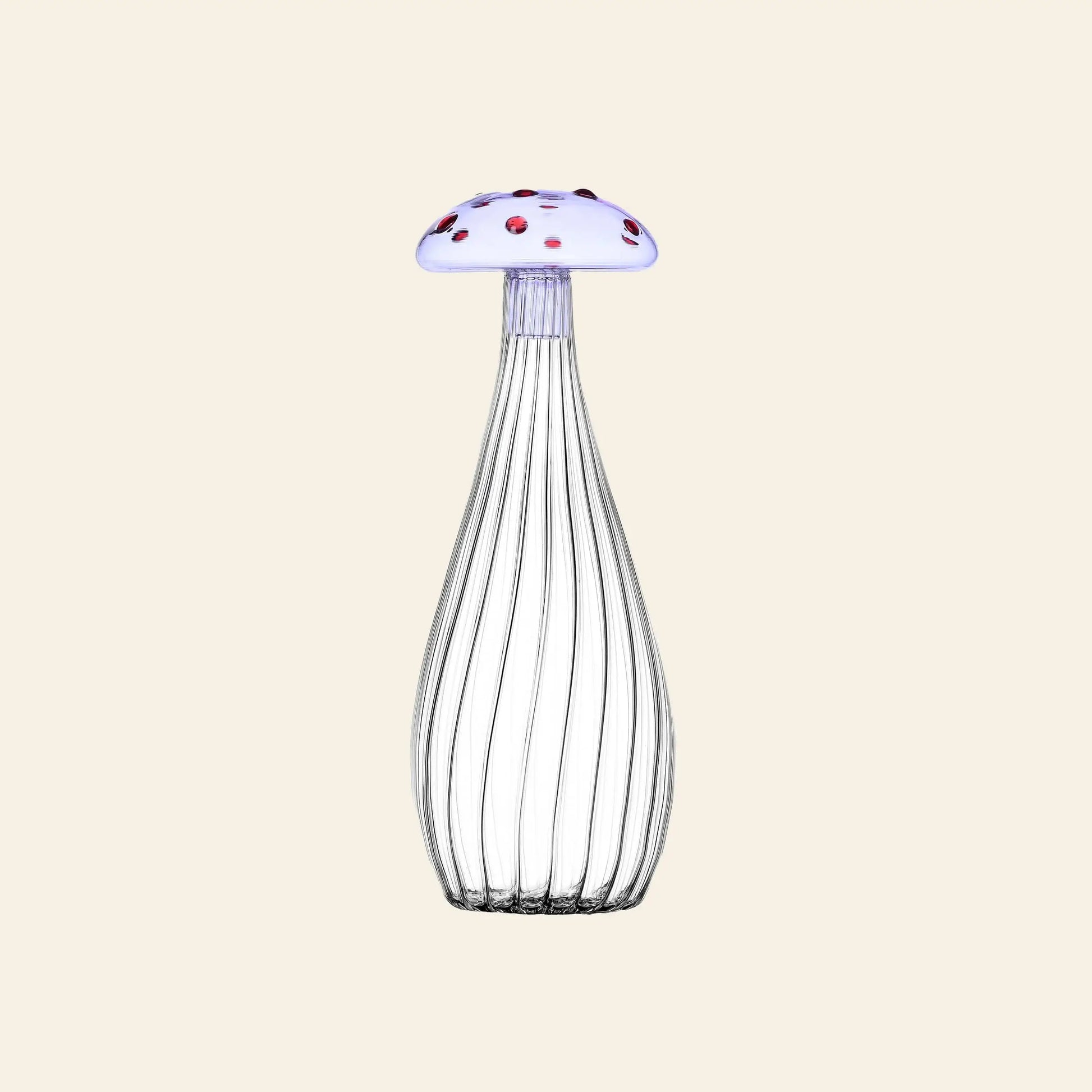 The Ichendorf Milano Alice Bottle by Ichendorf Milano features clear ribbed glass and a whimsical mushroom-shaped cap—white with red spots—set against a plain beige background.