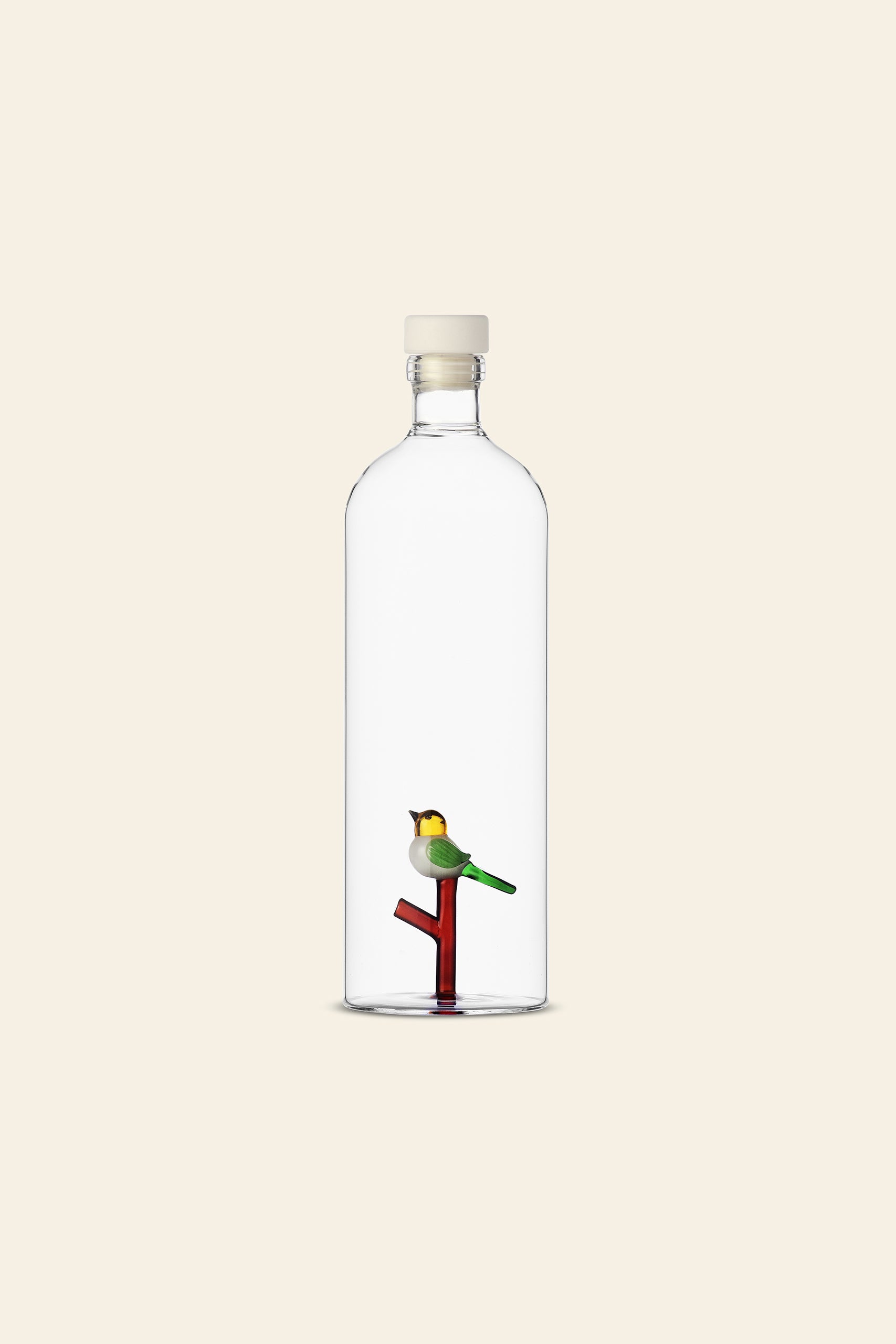 The Ichendorf Milano Animal Farm Bottle by Ichendorf Milano features a handcrafted glass design with a white cap, showcasing a small bird on a red and green branch inside, set against a plain light beige background.