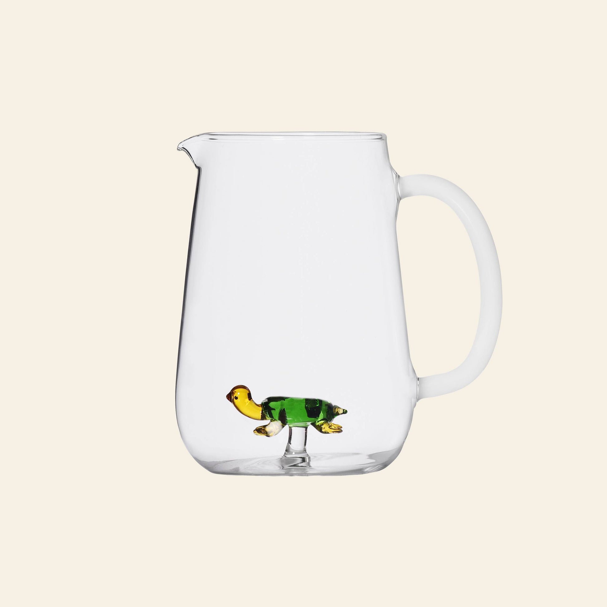The Ichendorf Milano Animal Farm Pitcher - Green Turtle features a clear glass body with handle and a small green glass turtle figurine inside, inspired by Alessandra Baldereschis collection. Shown against a plain, light background.