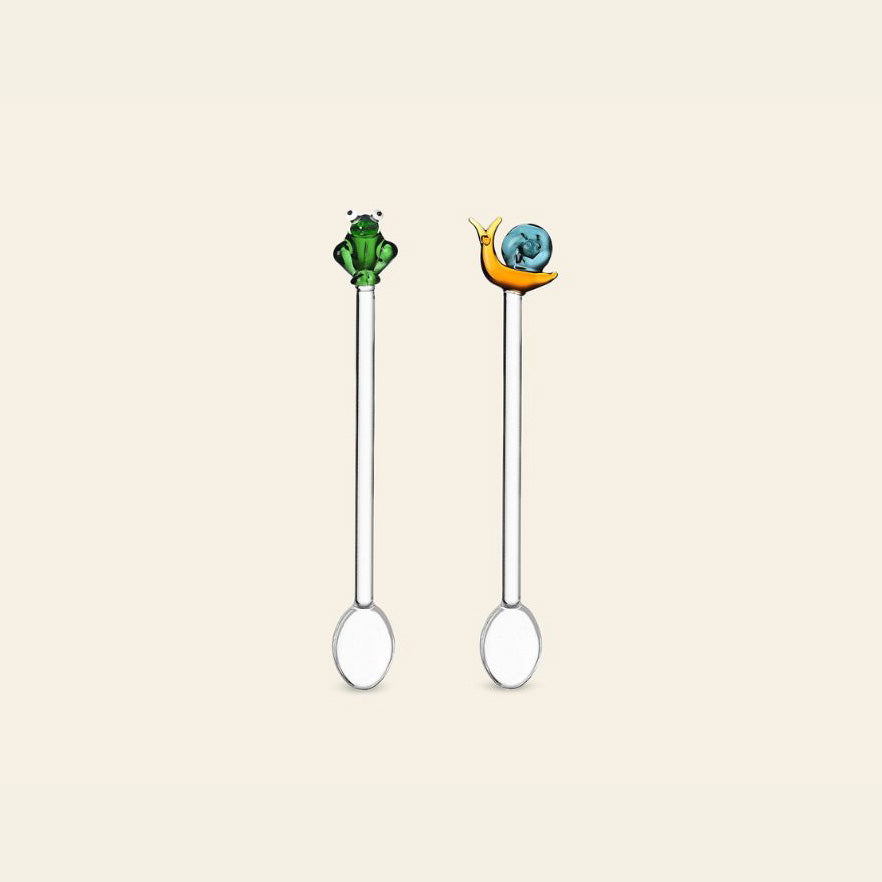 The Ichendorf Milano Animal Farm Spoons set features two metal spoons by Ichendorf Milano, one with a green frog and the other with an orange snail with a blue shell on the handles, shown against a plain light background.