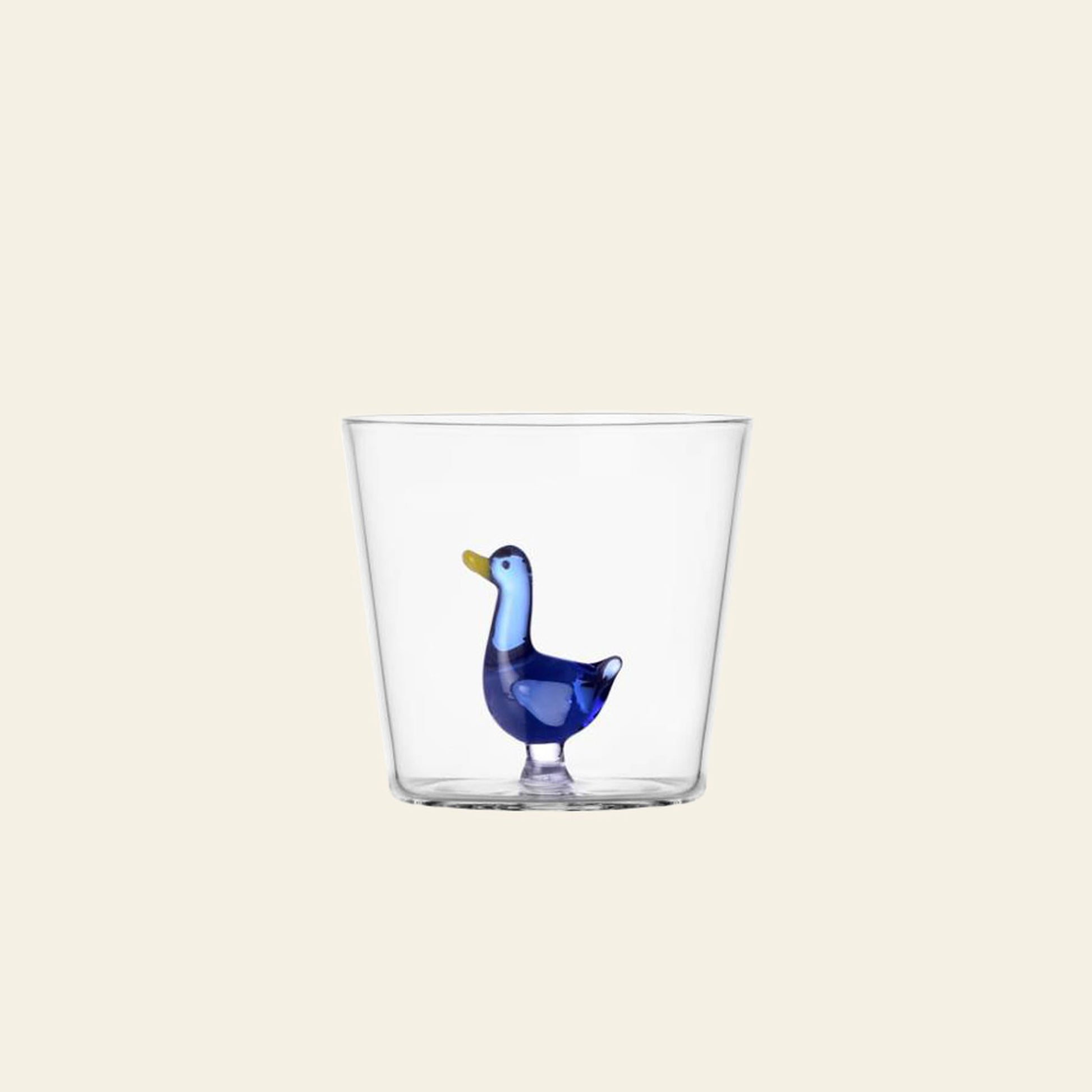 The Ichendorf Milano Animal Farm Tumbler by Ichendorf Milano features a clear glass design with a small blue glass duck inside, shown against a plain light beige background.