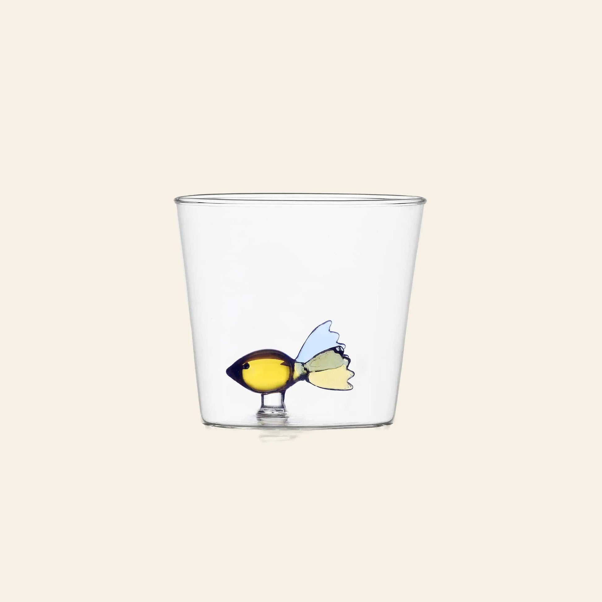 The Ichendorf Milano Animal Farm Tumbler by Ichendorf Milano is a clear handcrafted glass tumbler featuring a small, colorful glass fish with a yellow body and blue fins attached to the inside bottom. Perfect for adding whimsy to your table.