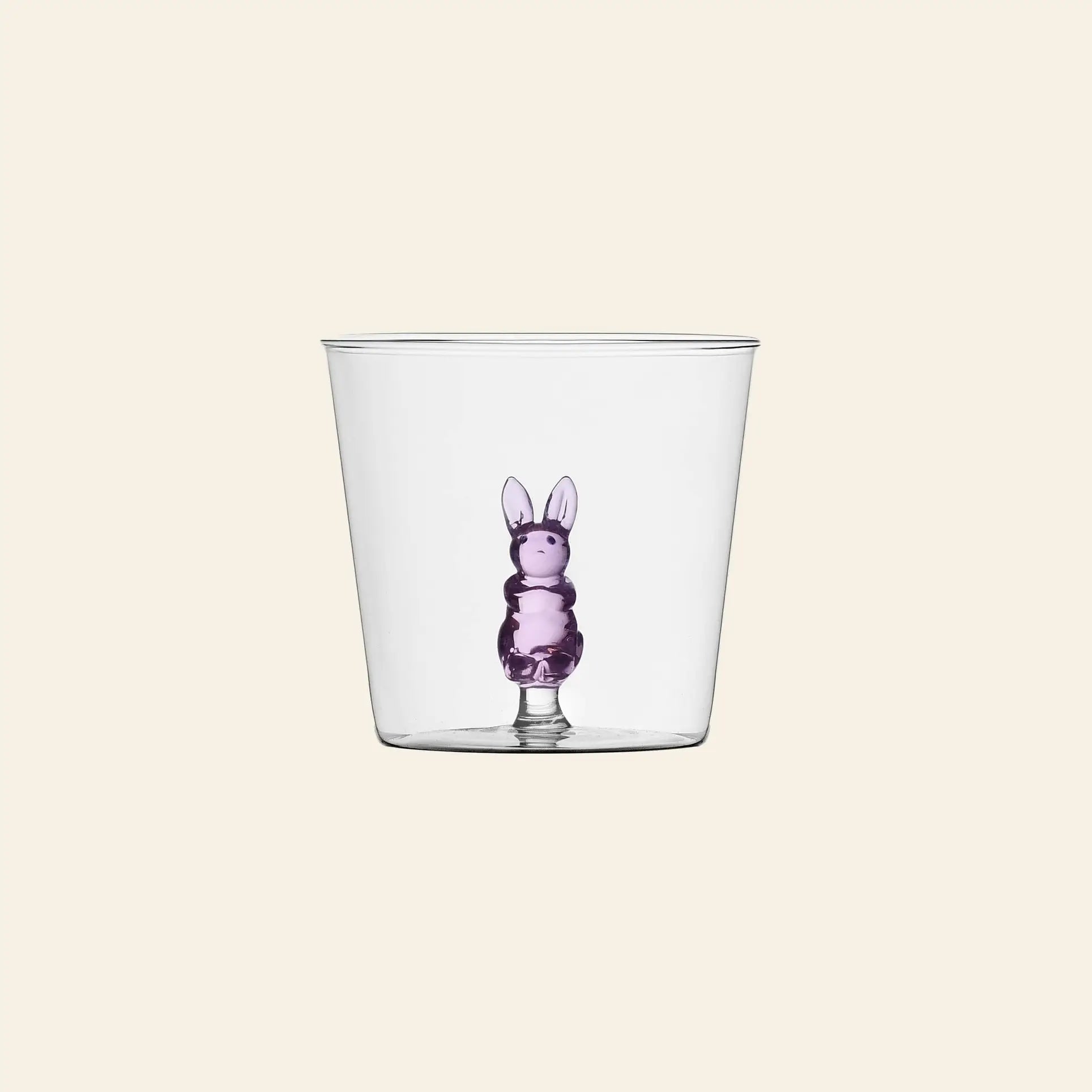 The Ichendorf Milano Animal Farm Tumbler by Ichendorf Milano features a whimsical clear glass design with a small purple bunny figure nestled at the base, set against a plain light background.