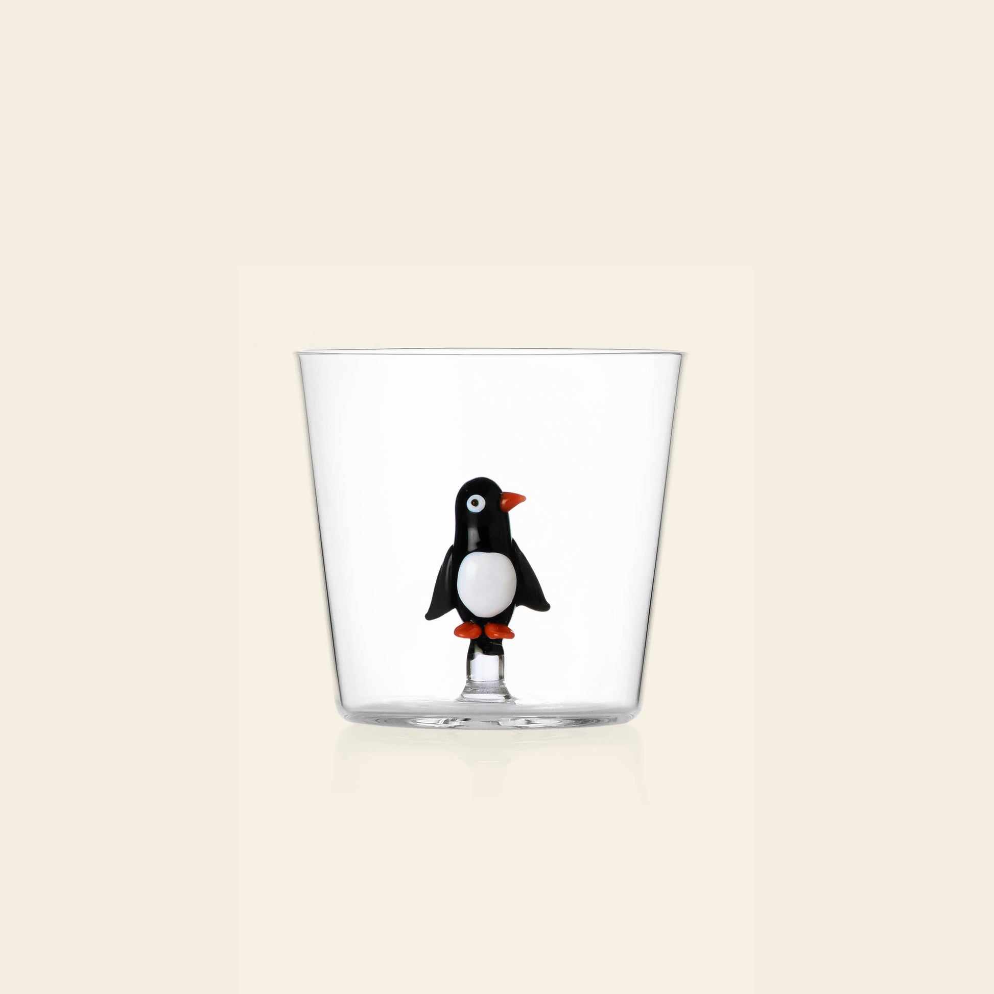 The Ichendorf Milano Christmas Tales Tumbler is a clear glass featuring a small 3D black and white penguin with an orange beak and feet at the bottom—an ideal festive holiday gift from Ichendorf Milano.