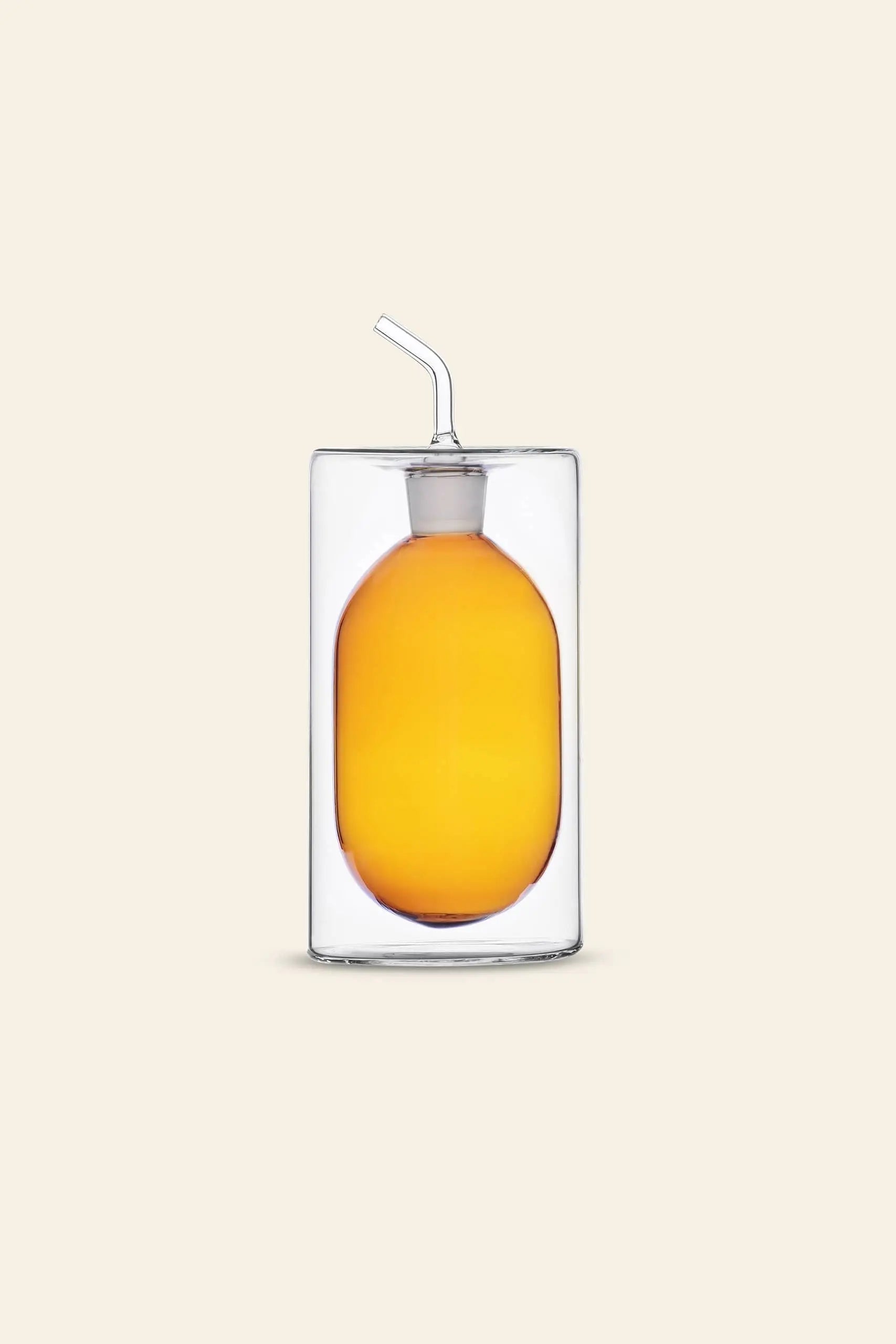 An orange drink in a glass with a bent straw holds an egg-shaped object resembling the Ichendorf Milano Cilindro Oil Bottle by Ichendorf Milano, creating a striking effect against a light beige background.