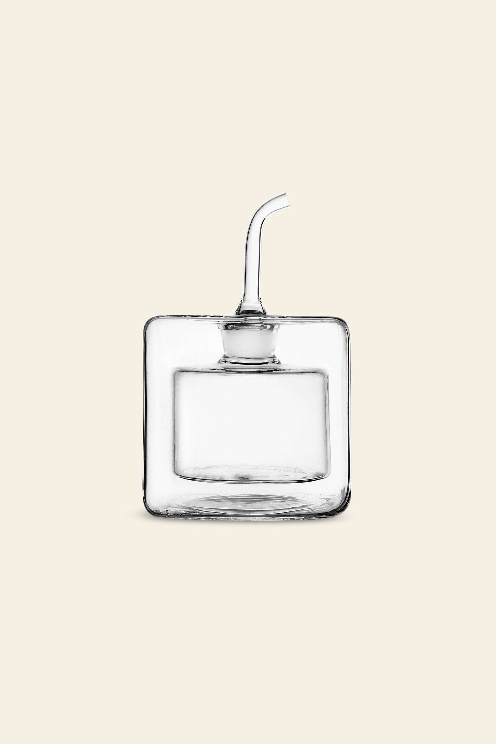 The Ichendorf Milano Cube Square Doublewalled Oil Bottle by Ichendorf Milano, with its clear, square design and curved spout, is elegantly displayed on a light beige background—combining modern style and smart function for olive oil storage.