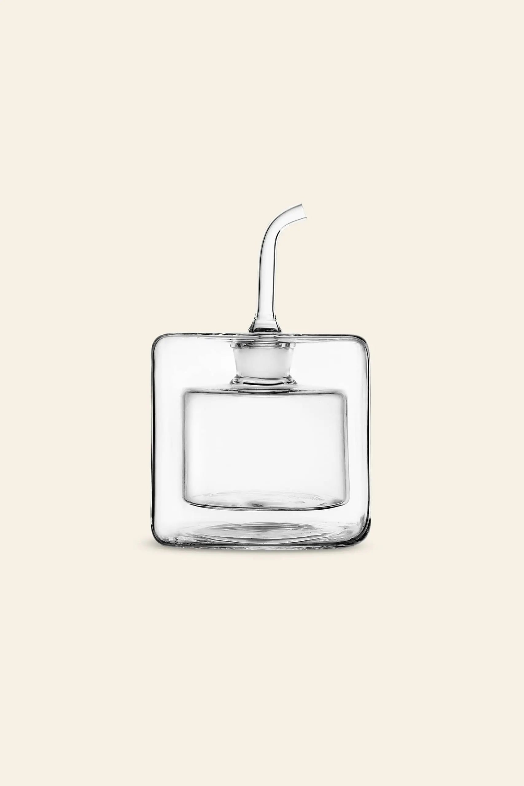 The Ichendorf Milano Cube Square Doublewalled Oil Bottle by Ichendorf Milano is a handcrafted, clear, square kitchenware piece with a short angled spout for olive oil, displayed on a plain beige background.