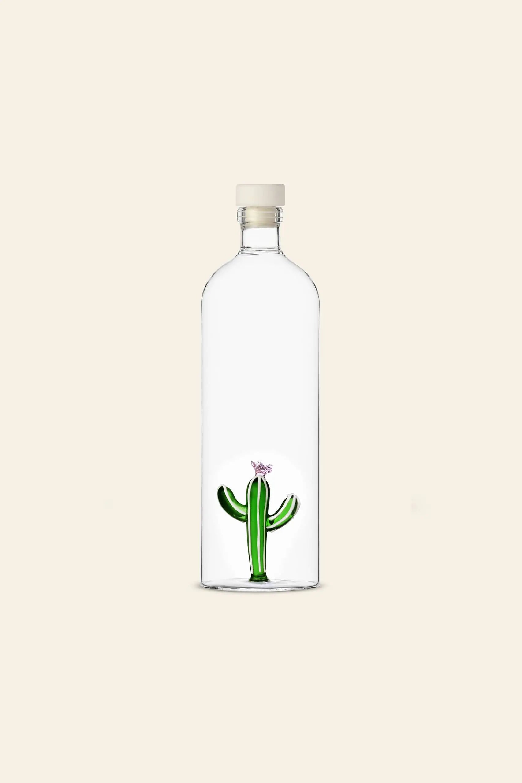 The Ichendorf Milano Desert Plants Bottle by Ichendorf Milano features a clear glass bottle with a beige cap, housing a small green cactus with a pink flower, set against a light beige background—a delightful desert-themed decor piece.