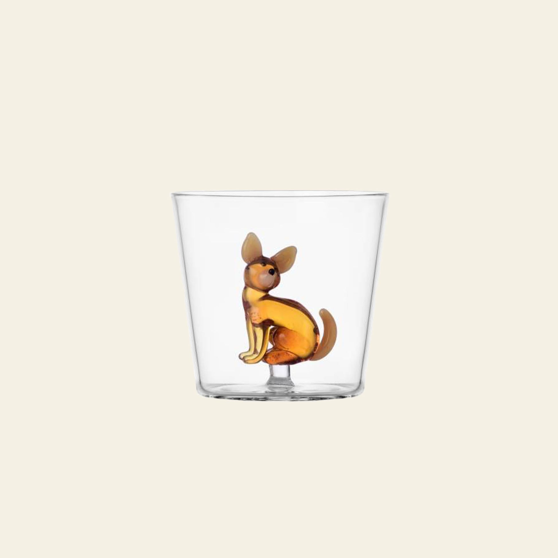 The Ichendorf Milano Dogs Tumbler - Chihuahua by Ichendorf Milano is a clear glass tumbler featuring a small brown and yellow sculpted Chihuahua figurine inside the base, shown against a plain light beige background.