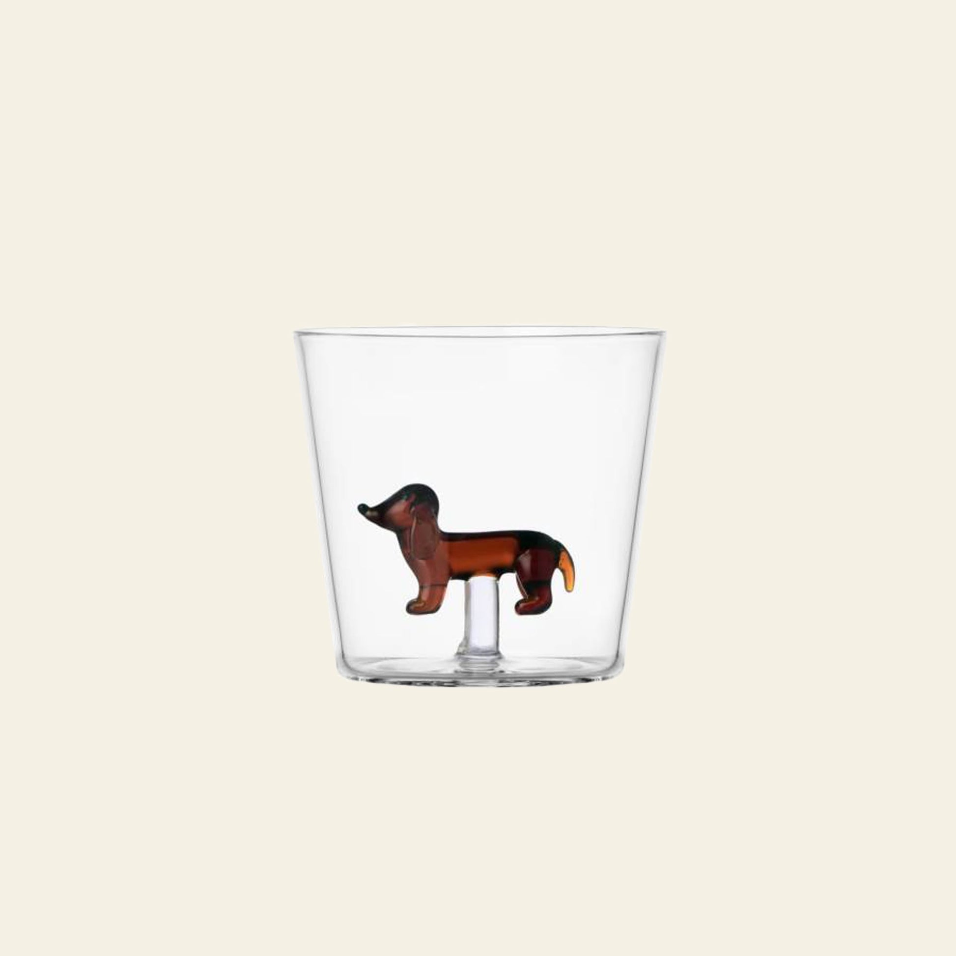 The Ichendorf Milano Dogs Tumbler - Dachshund by Ichendorf Milano features a clear glass design with a small brown dachshund figurine affixed to the inside bottom of the cup, set against a plain light background.