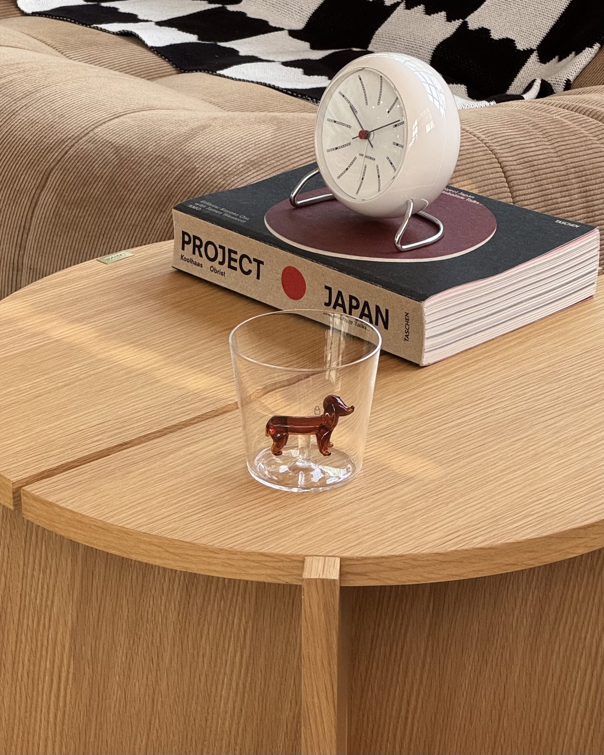 An Ichendorf Milano Dogs Tumbler - Dachshund by Ichendorf Milano rests on a wooden table beside Project Japan and a round white clock with red hands.