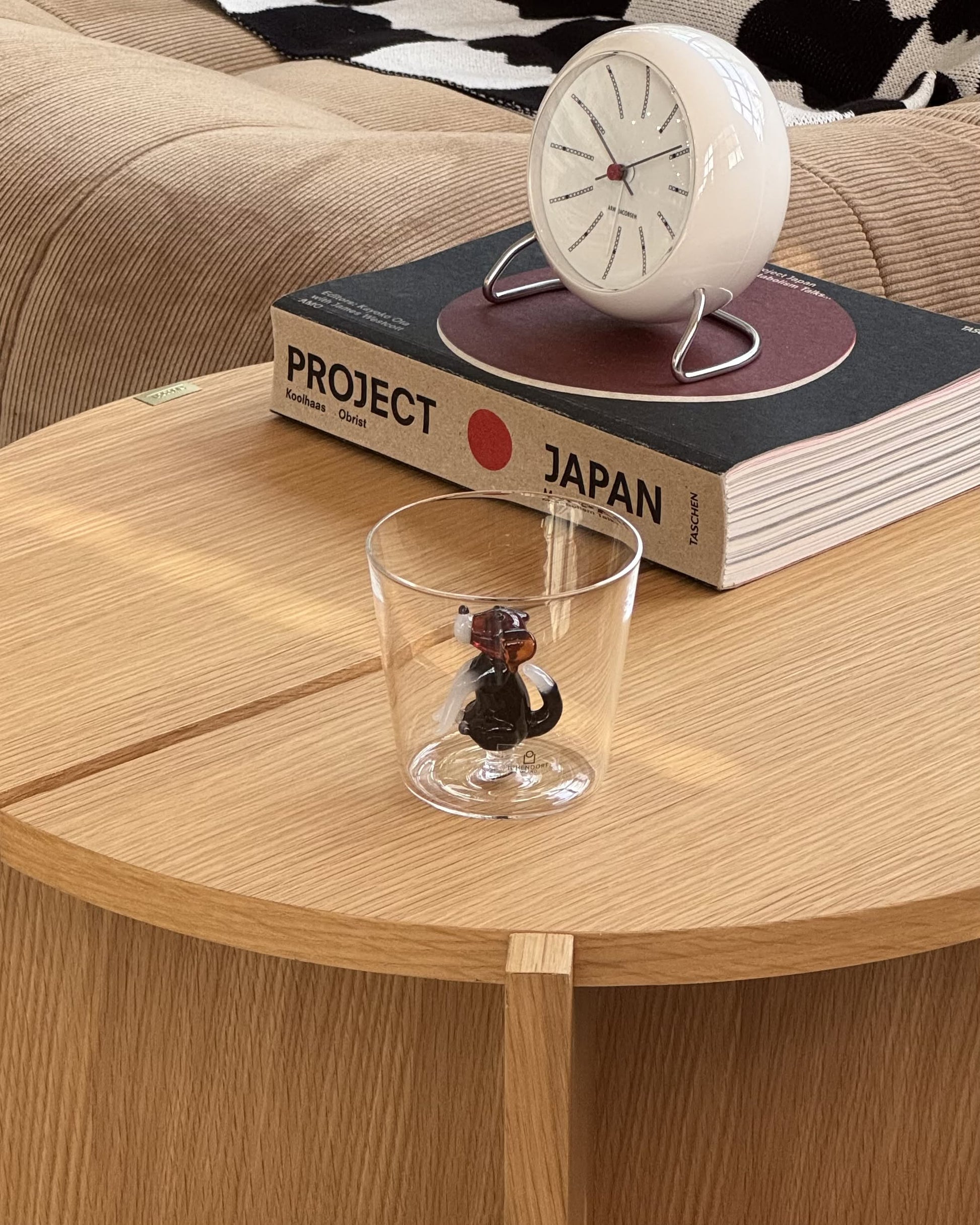 An Ichendorf Milano Dogs Tumbler - English Foxhound sits on a wooden table, with PROJECT JAPAN and a white clock behind it. In the background are a beige sofa and a black-and-white pillow.
