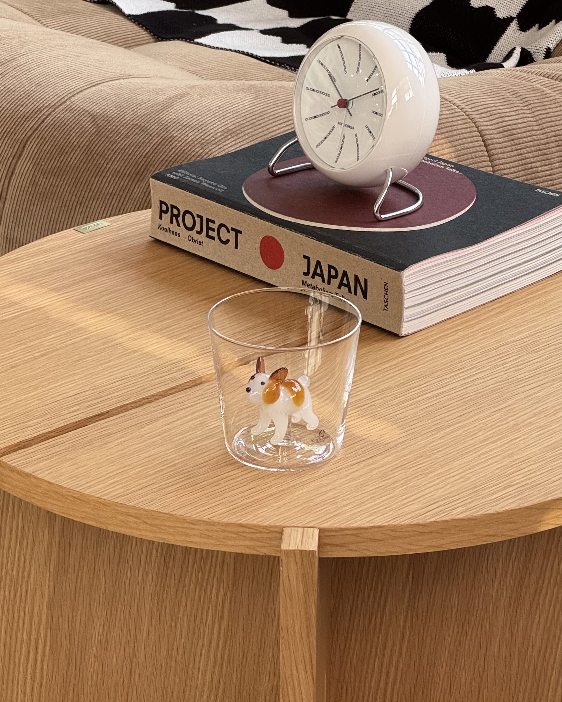 The Ichendorf Milano Dogs Tumbler - French Bulldog, a handcrafted glass by Ichendorf Milano featuring a French Bulldog figurine, sits on a wooden table beside two books and a clock.