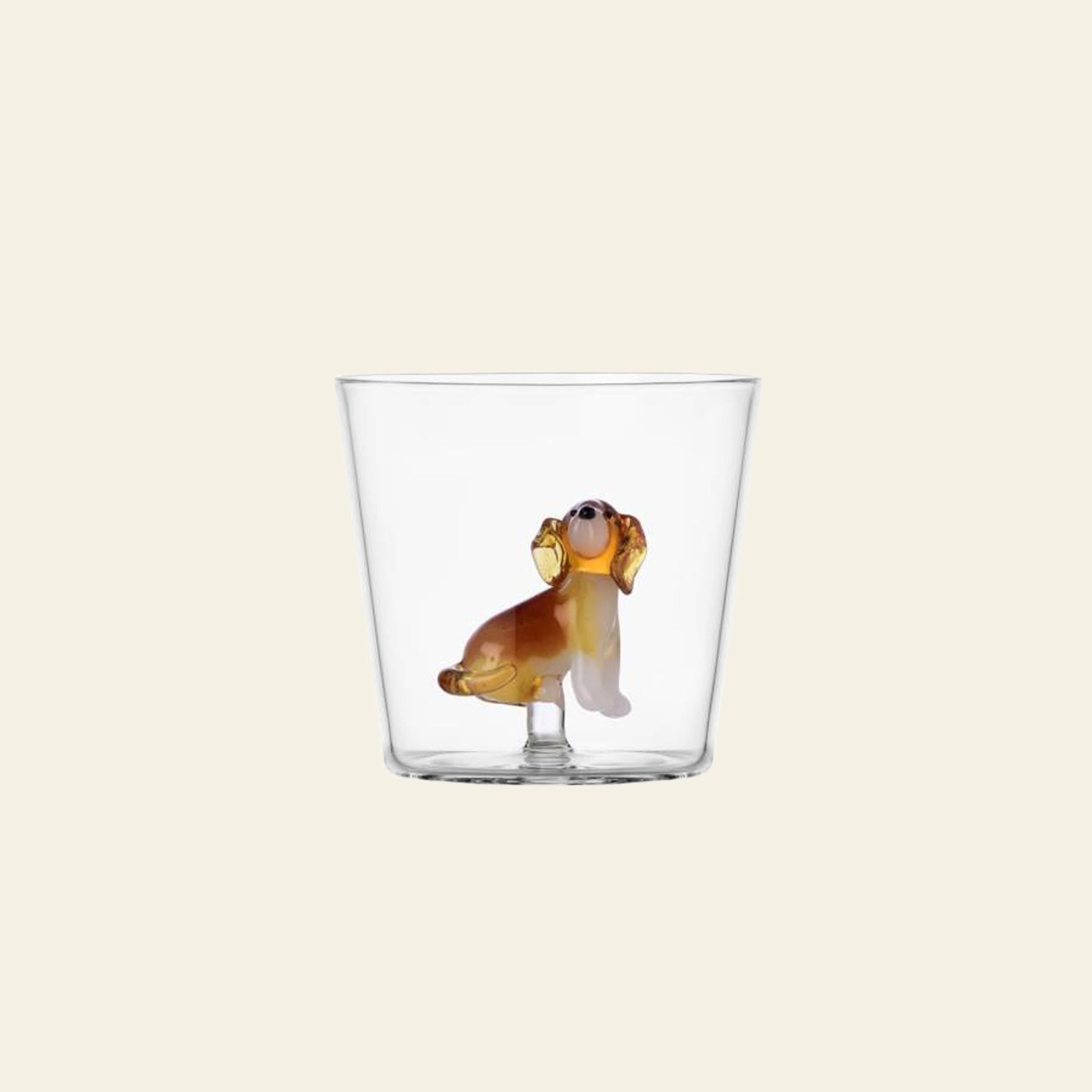 The Ichendorf Milano Dogs Tumbler - Golden Retriever is a clear handcrafted glass by Ichendorf Milano, featuring a small Golden Retriever figurine at the bottom, shown on a plain beige background.