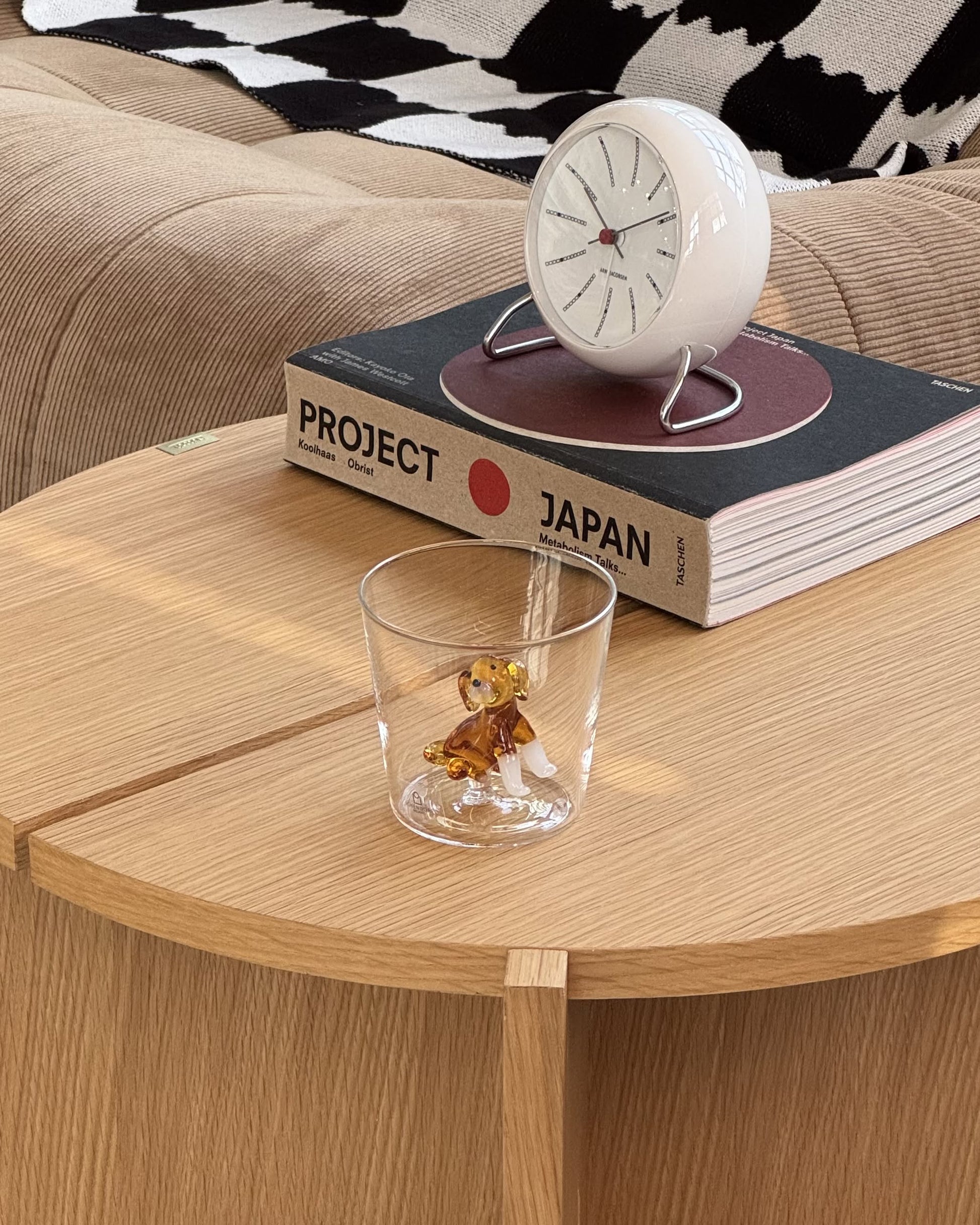 The Ichendorf Milano Dogs Tumbler - Golden Retriever features a handcrafted glass with a golden retriever figurine inside, shown on a wooden table beside a “PROJECT JAPAN” book, round clock, and beige couch in the background.