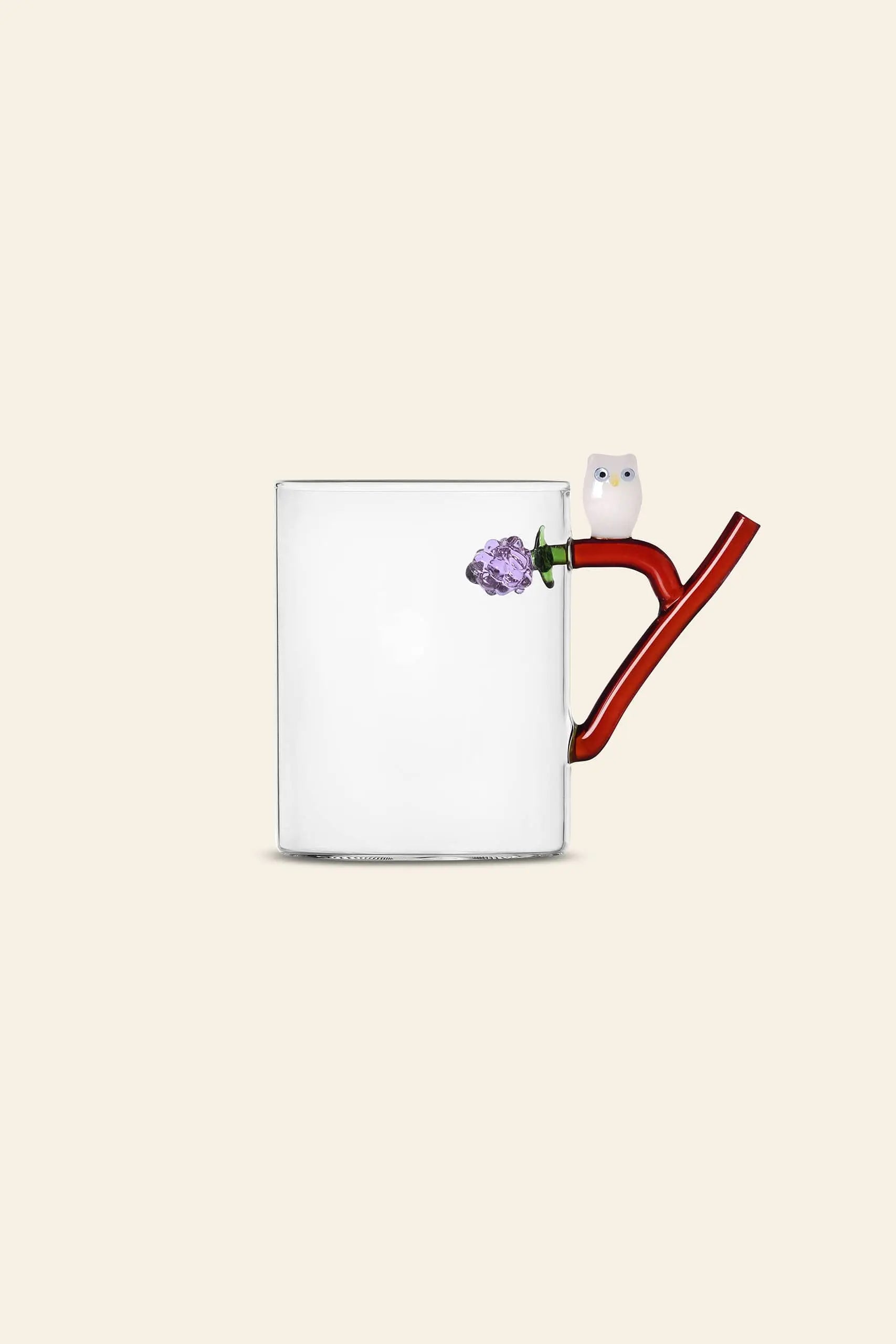 The Ichendorf Milano Fruits and Flower Mug features a clear glass body, a red branch handle with a white owl and purple flower, from the whimsical collection by Alessandra Baldereschi, set against a plain beige background.