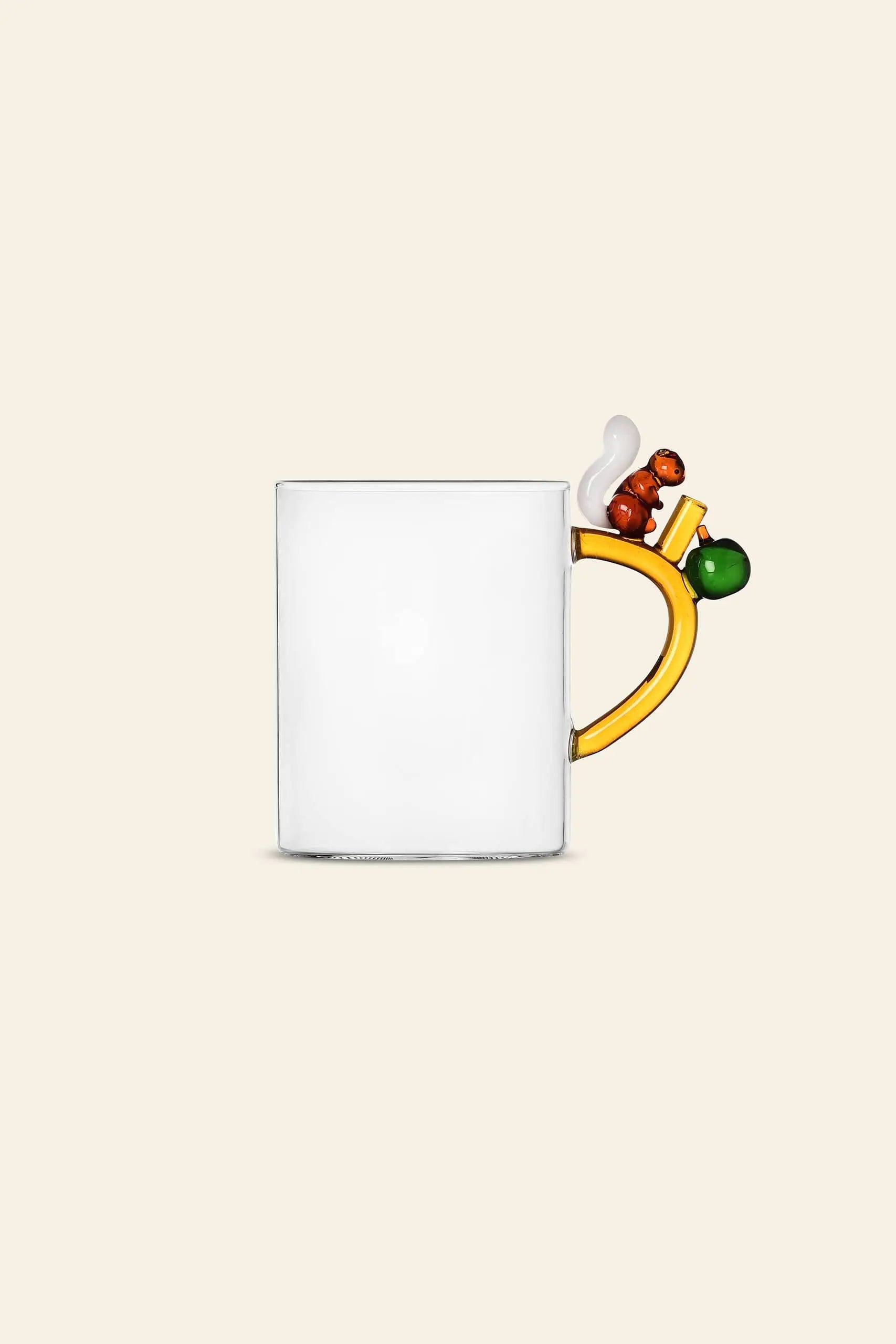 The Ichendorf Milano Fruits and Flower Mug by Ichendorf Milano features clear glass, a whimsical yellow handle, brown squirrel, white swirl, green ball, and orange geometric accent set against a plain beige background.