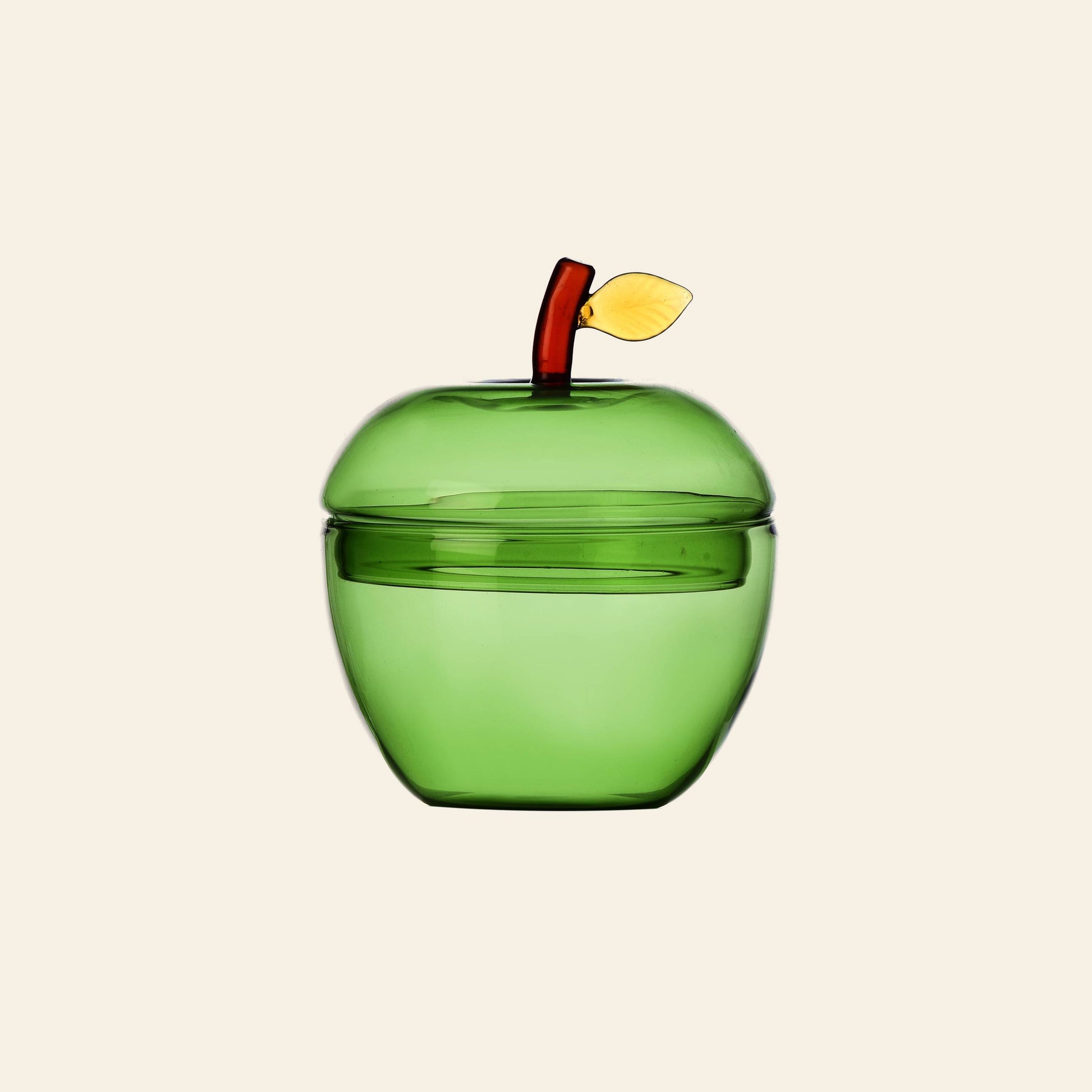 The Ichendorf Milano Fruits and Flowers Sugar Bowl, a green glass apple with red stem and yellow leaf, by Ichendorf Milano, sits on a light beige background, celebrating the playful charm of colourful fruits.