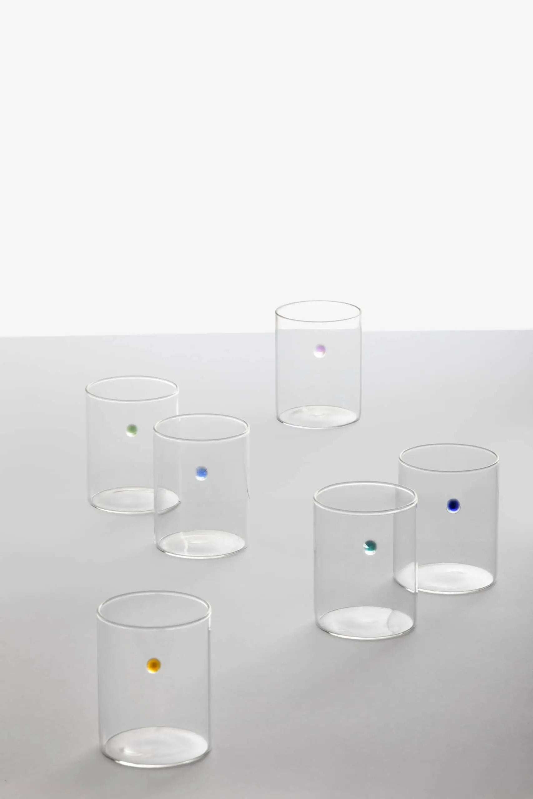 The Ichendorf Milano Soleils Tumbler Set of 6 features handcrafted glassware, each accented with a single colored dot—yellow, green, blue, purple, turquoise, and dark blue—displayed on a white surface against a plain light background.