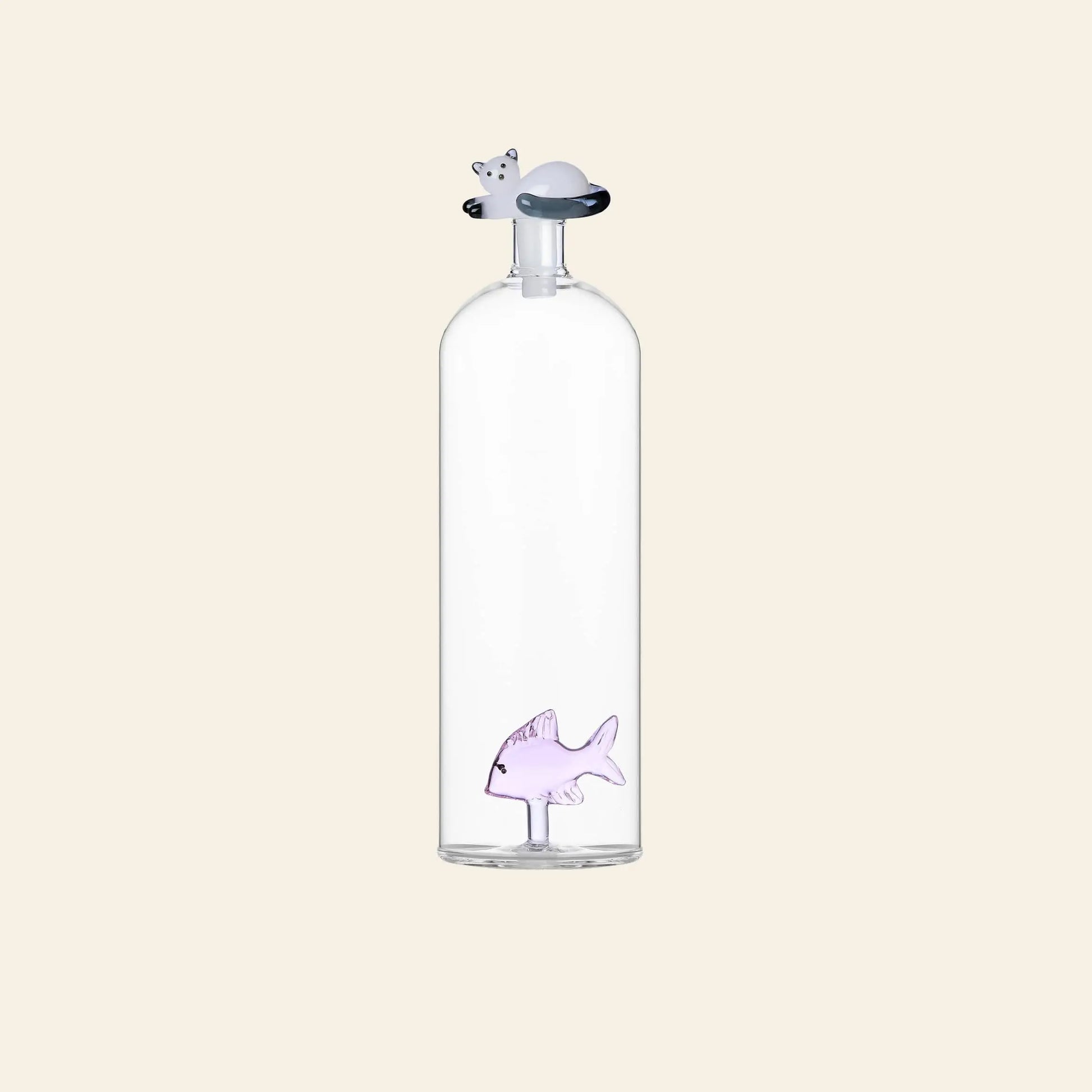 The Ichendorf Milano Tabby Cat Bottle by Ichendorf Milano is a clear glass bottle with a small purple fish figurine inside and a cat-shaped stopper on top, shown against a plain light beige background.