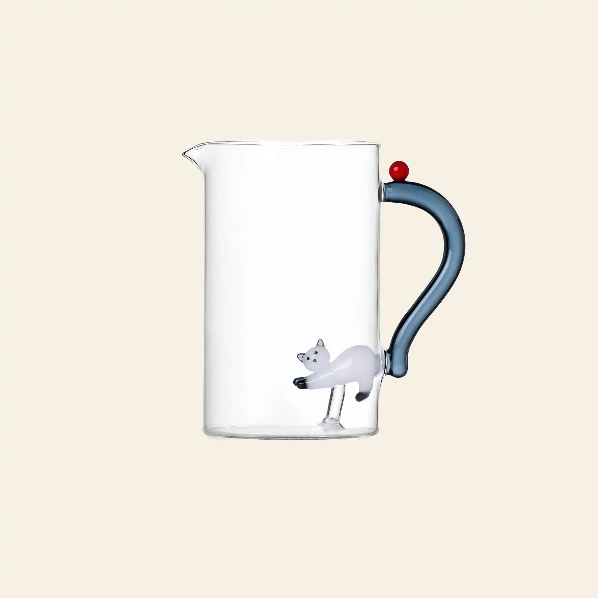 Add charm to your Tabby Cat collection with the Ichendorf Milano Tabby Cat Jug—a clear handcrafted jug by Ichendorf Milano, featuring a blue handle, red ball lid, and a small white cat figurine at the base.