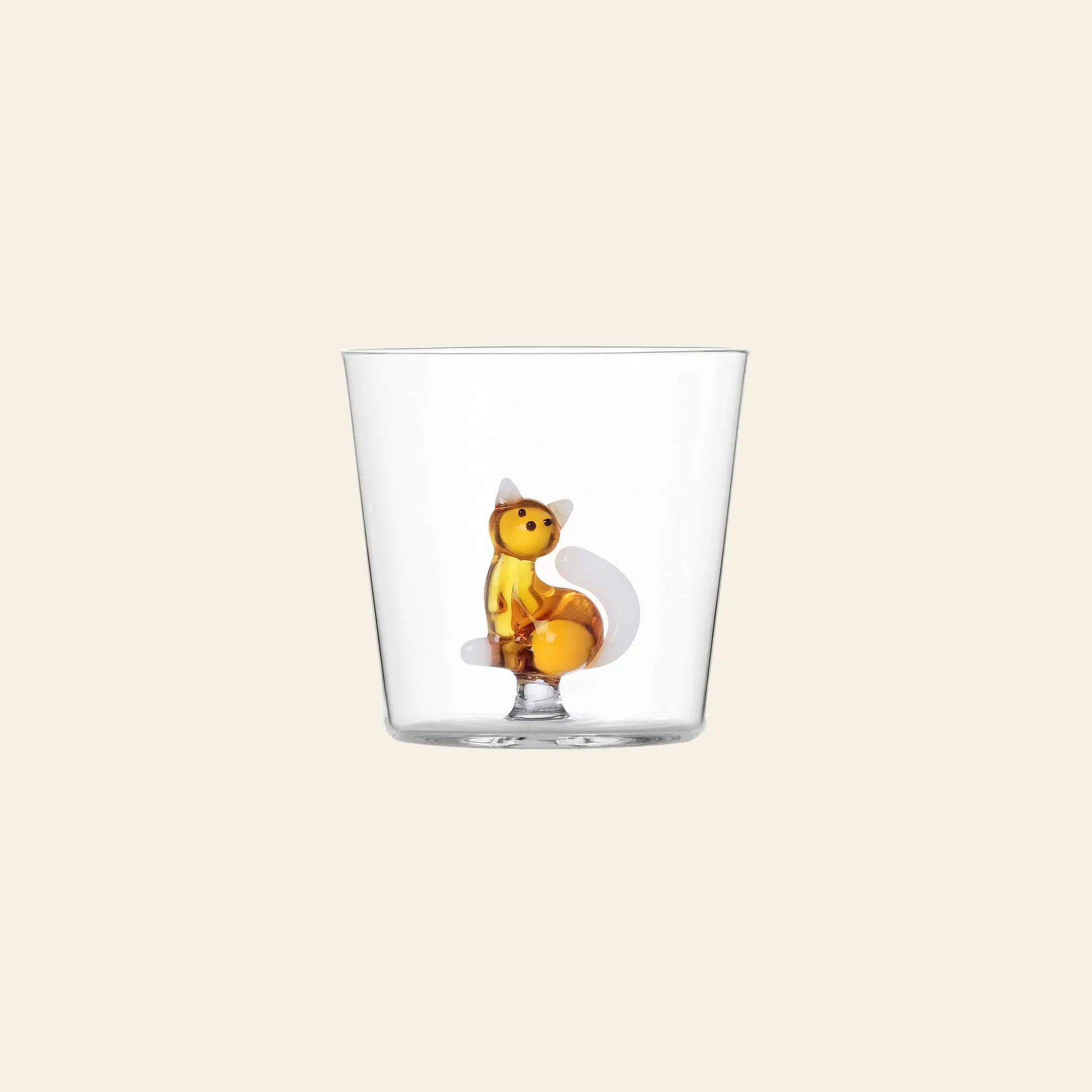 The Ichendorf Milano Tabby Cat Tumbler, by Ichendorf Milano, is a clear glass cup featuring a small upright orange fox figurine at the center, ideal for cat lovers and displayed on a plain beige background.