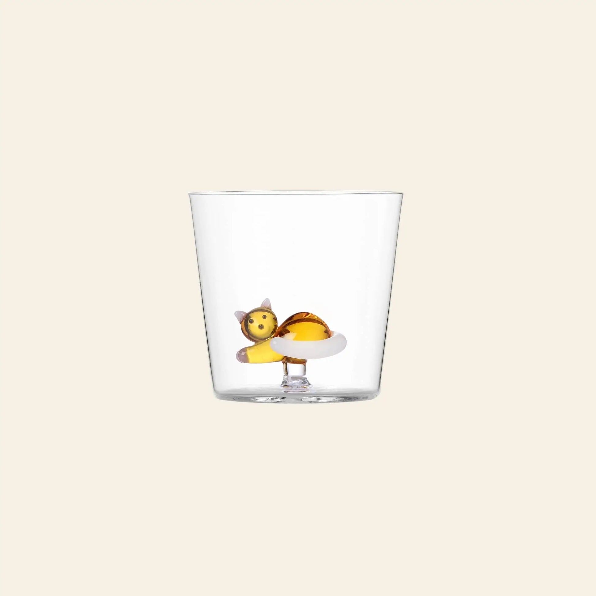The Ichendorf Milano Tabby Cat Tumbler features a small, colorful cat figurine lying at the bottom. This handcrafted clear glass by Ichendorf Milano is perfect for cat lovers and stands out against a plain, light-colored background.
