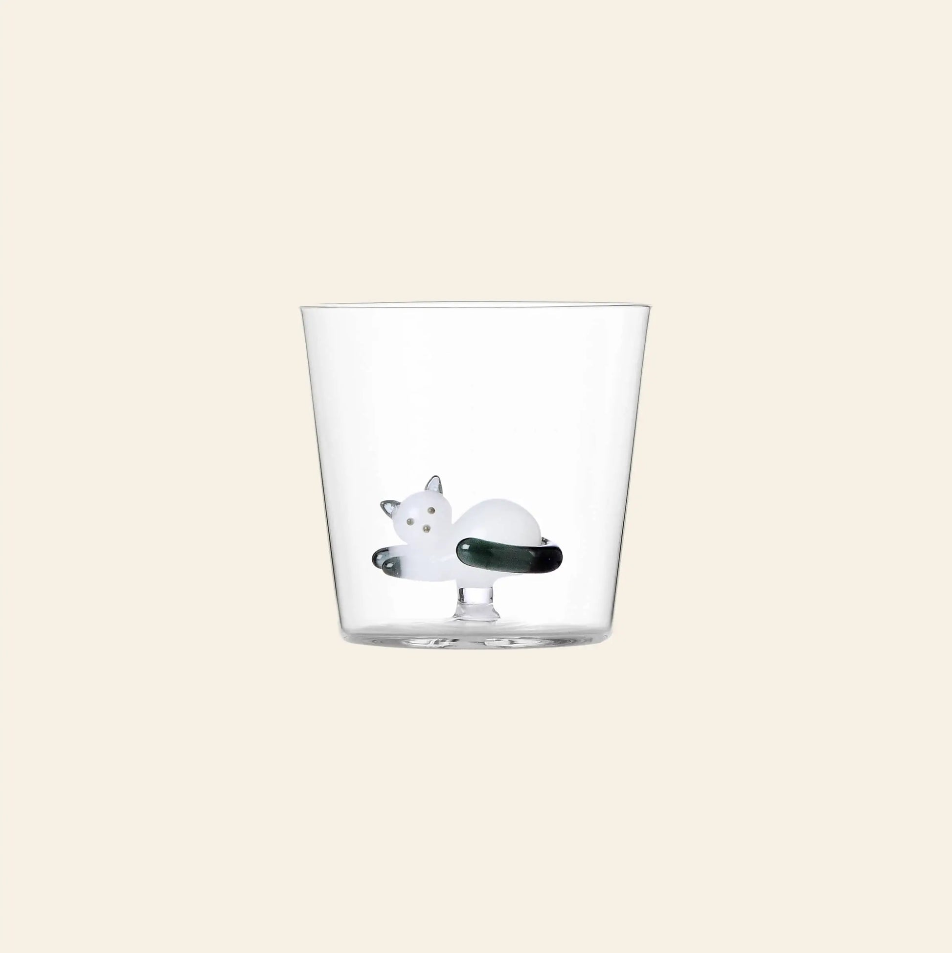 The Ichendorf Milano Tabby Cat Tumbler features a small white glass cat curled up at the bottom—a charming piece from Ichendorf Milano, perfect for cat lovers. Shown against a plain beige background.