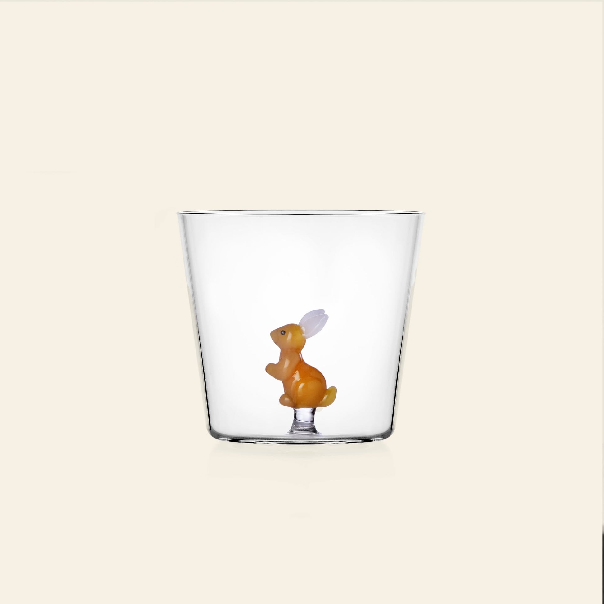 The Ichendorf Milano Woodland Tales Tumbler by Ichendorf Milano is a clear glass featuring a small orange rabbit with white ears at its base, displayed on a plain, light beige background.
