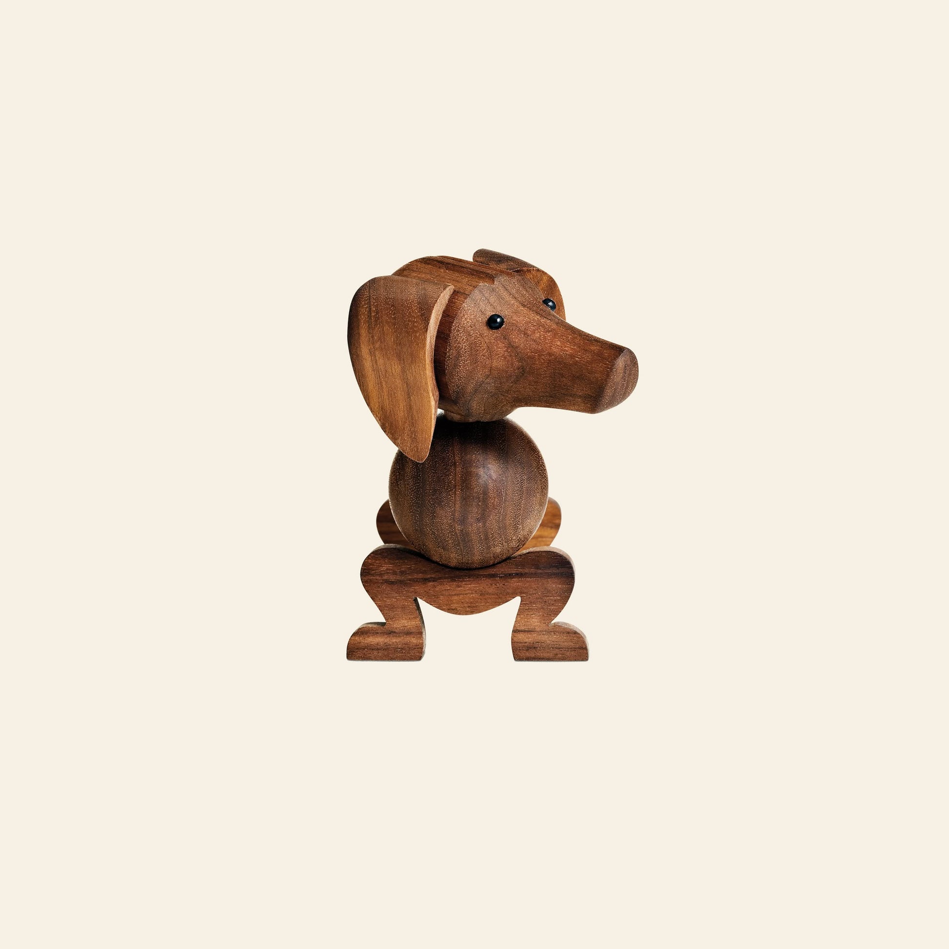 The Kay Bojesen Dog Small by Kay Bojesen is a carved wooden figurine with exaggerated ears and a rounded body, presented against a plain, light beige background—a true design icon.