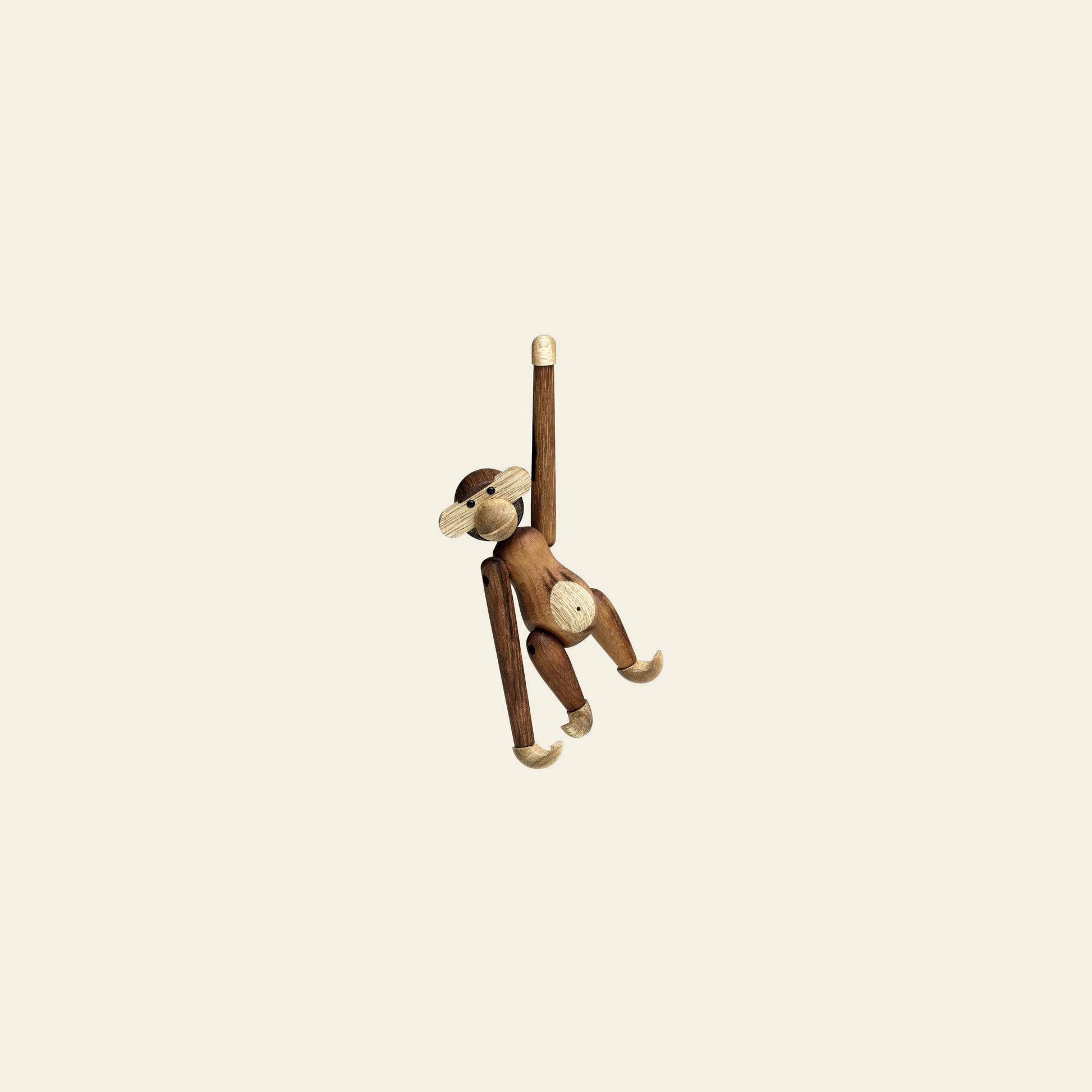 The Kay Bojesen Monkey Mini by Kay Bojesen hangs playfully by one arm against a light beige background, creating a delightful collectible keepsake.
