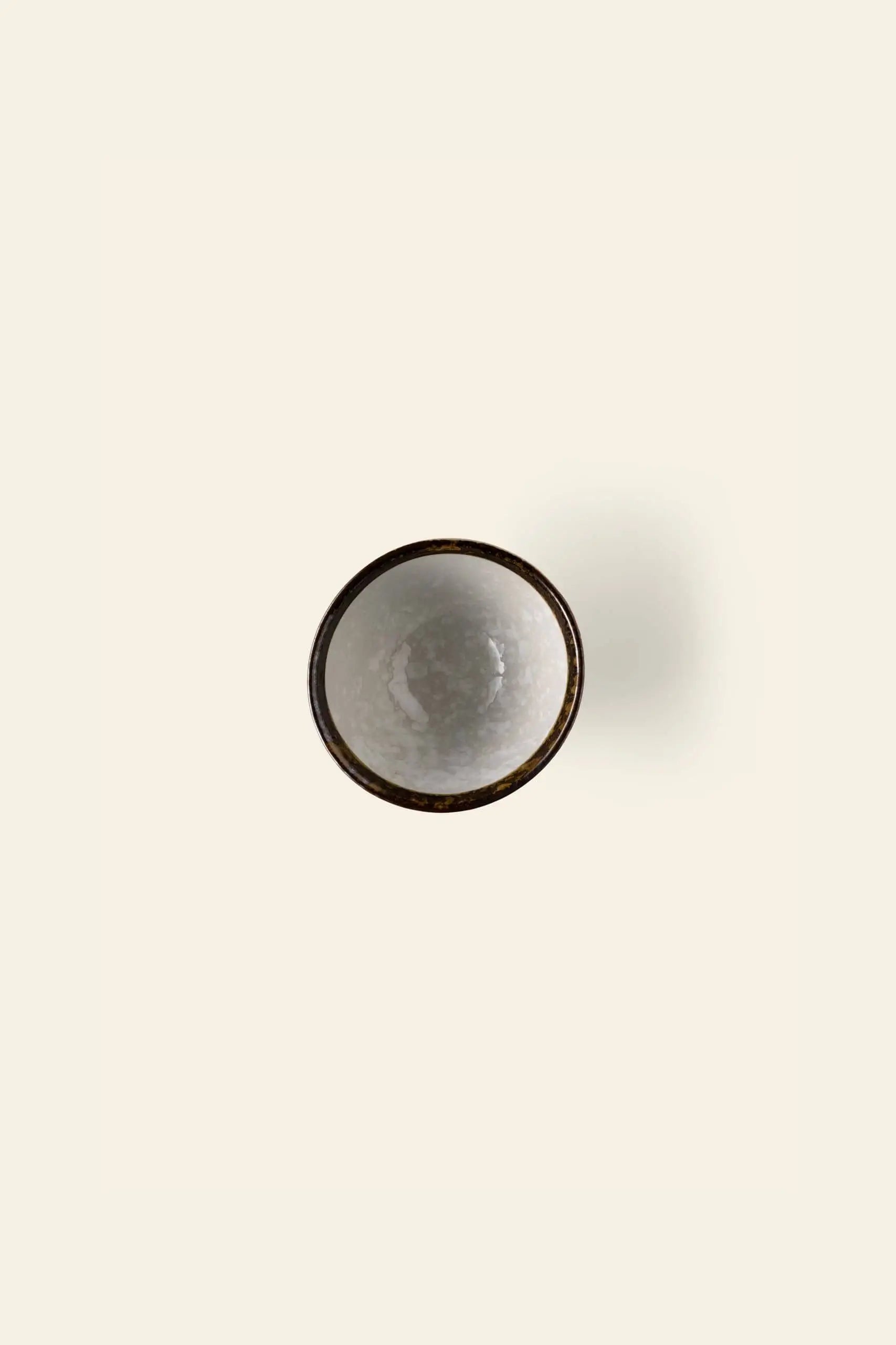 The Kra Sanctuary Satay Everyday Rice Bowl by Kra Sanctuary, a small round ceramic bowl filled with white liquid and viewed from above, is centered on a plain off-white background—bringing elegance to any dining experience.