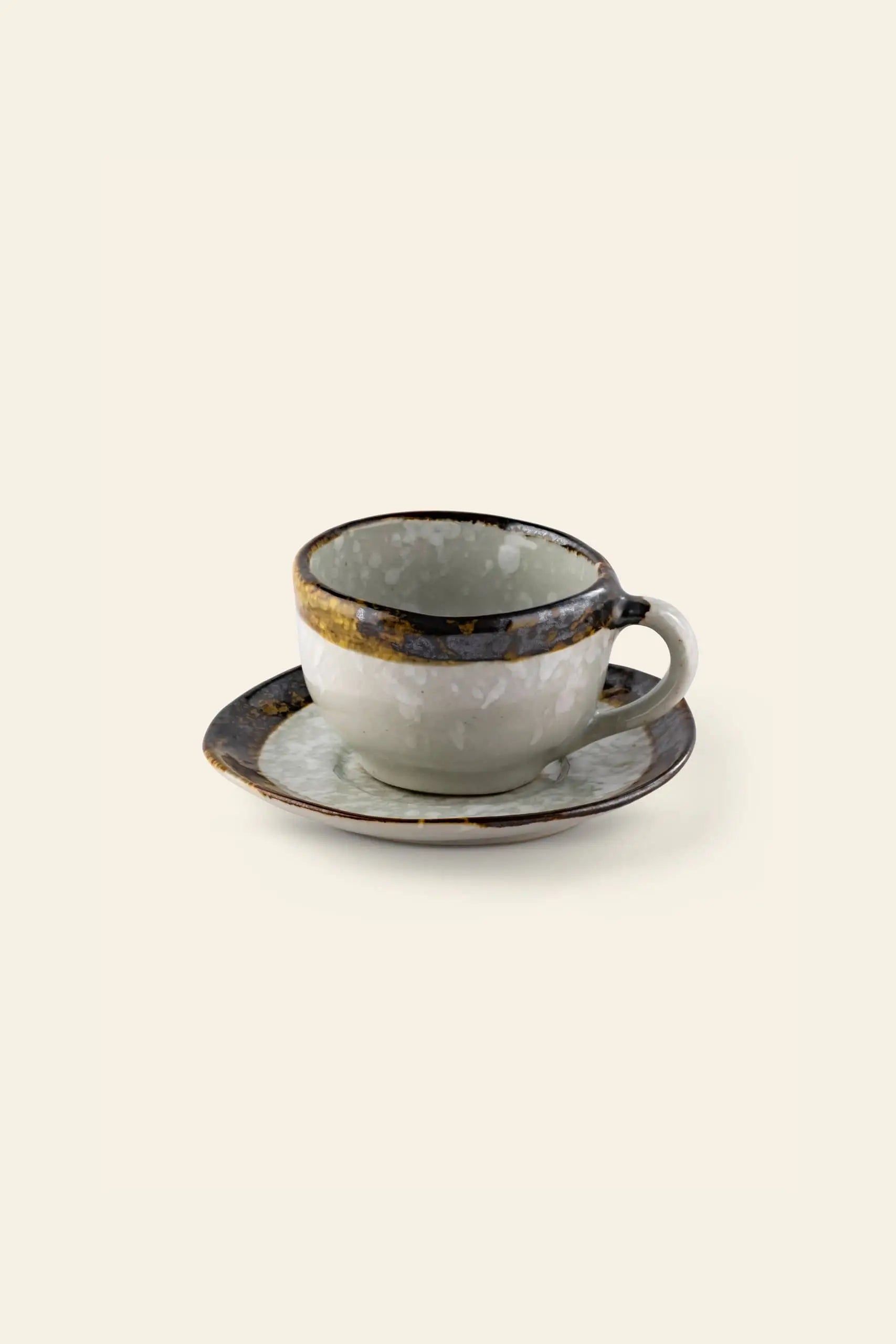 The Kra Sanctuary Satay Free-Form Cup and Coaster features a handle, mottled dark and light glaze, and an iridescent border—perfect against a plain background to enhance your earthy dinnerware collection.