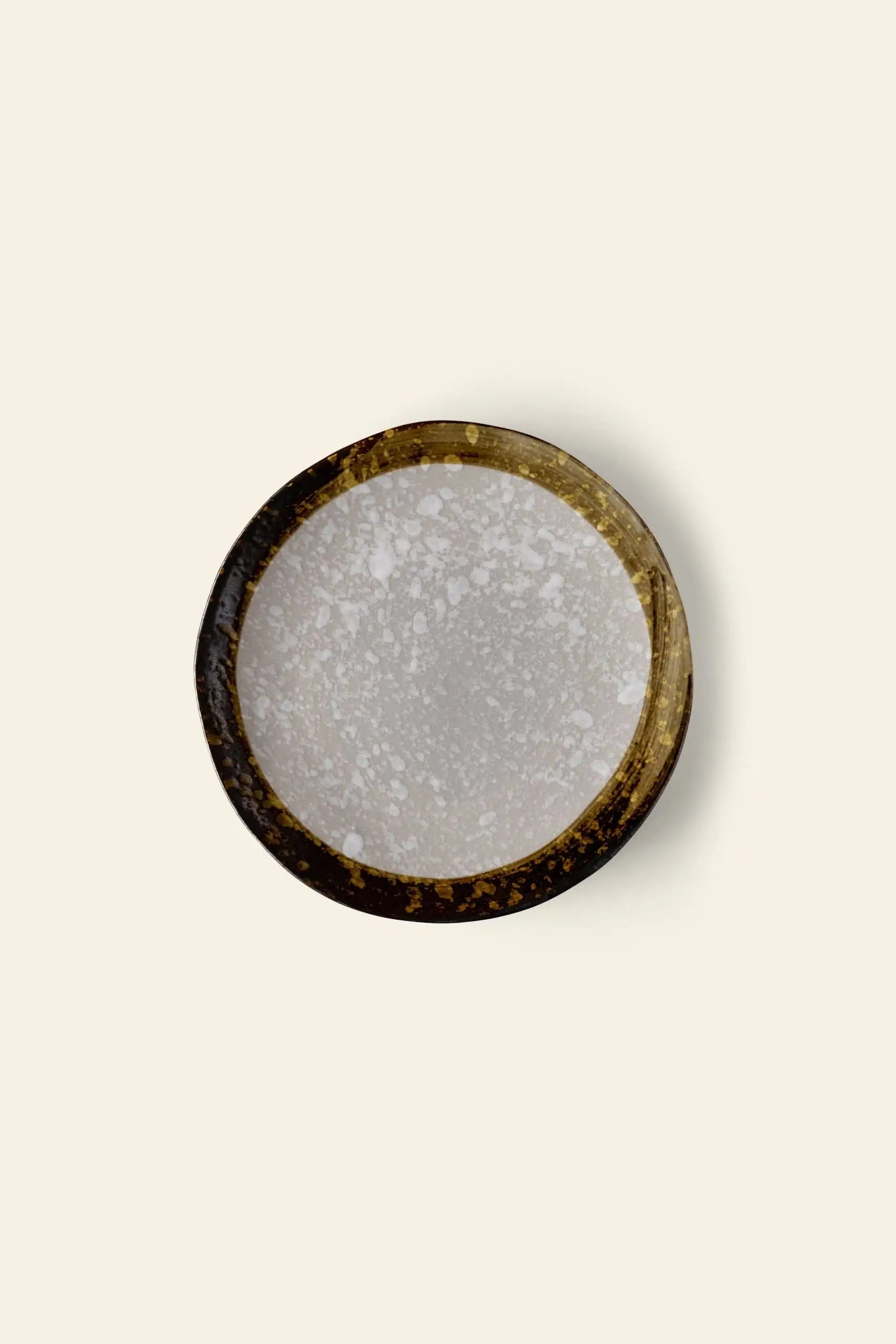The Kra Sanctuary Satay Free-Form Dinner Plate by Kra Sanctuary is a round ceramic plate with a brown textured rim and speckled light gray center, seen from above on a plain off-white background.
