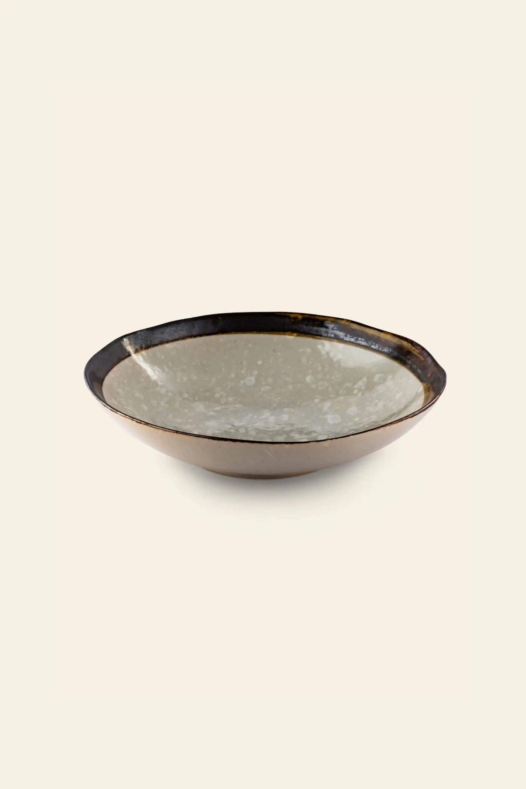 The Kra Sanctuary Satay Free-Form Pasta Bowl is a shallow, round ceramic bowl with a glossy, speckled light gray interior and dark brown rim and exterior, perfect for elevating your dining experience. Brand: Kra Sanctuary.