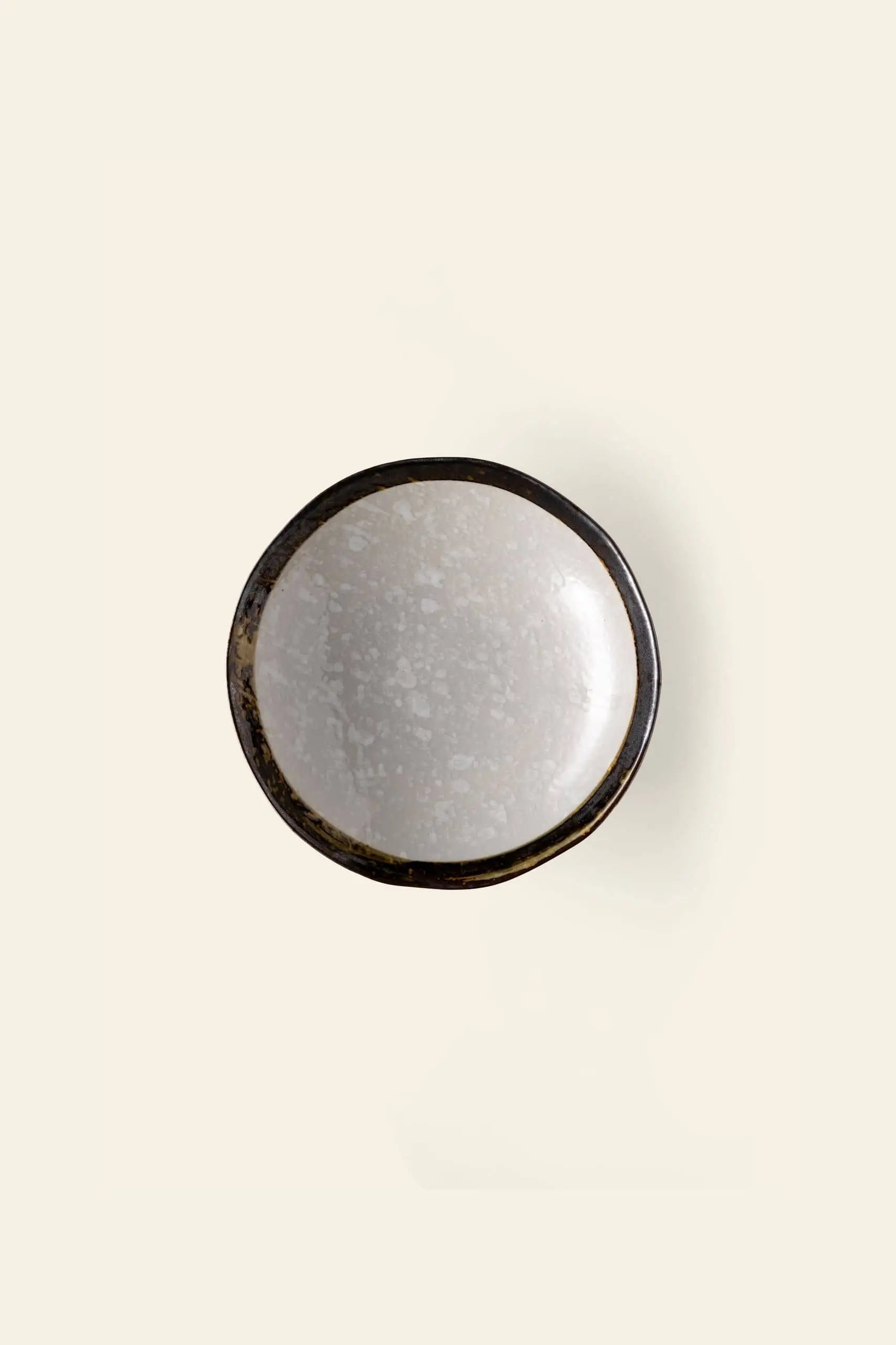 The Kra Sanctuary Satay Free-Form Pasta Bowl by Kra Sanctuary features a round, shallow design with a dark, uneven rim and light speckled interiorโphotographed from above on an off-white backgroundโideal for elevating your dining experience.
