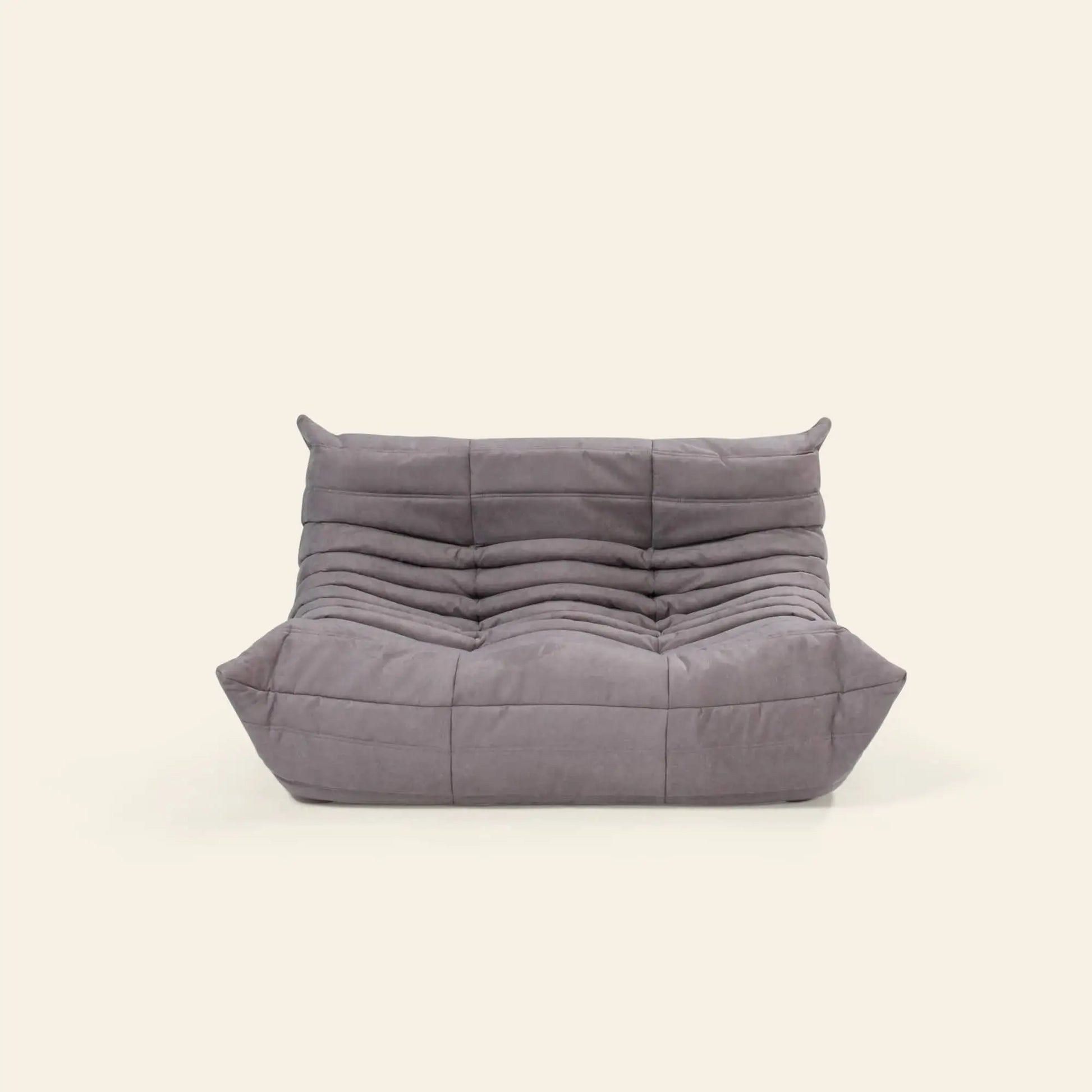 The Ligne Roset Togo, 2 Seater by Ligne Roset is a modern, low-profile gray sofa with a quilted, tufted design and deep cushioned seat and backrest, inspired by mid-century style—ideal against a plain light background.