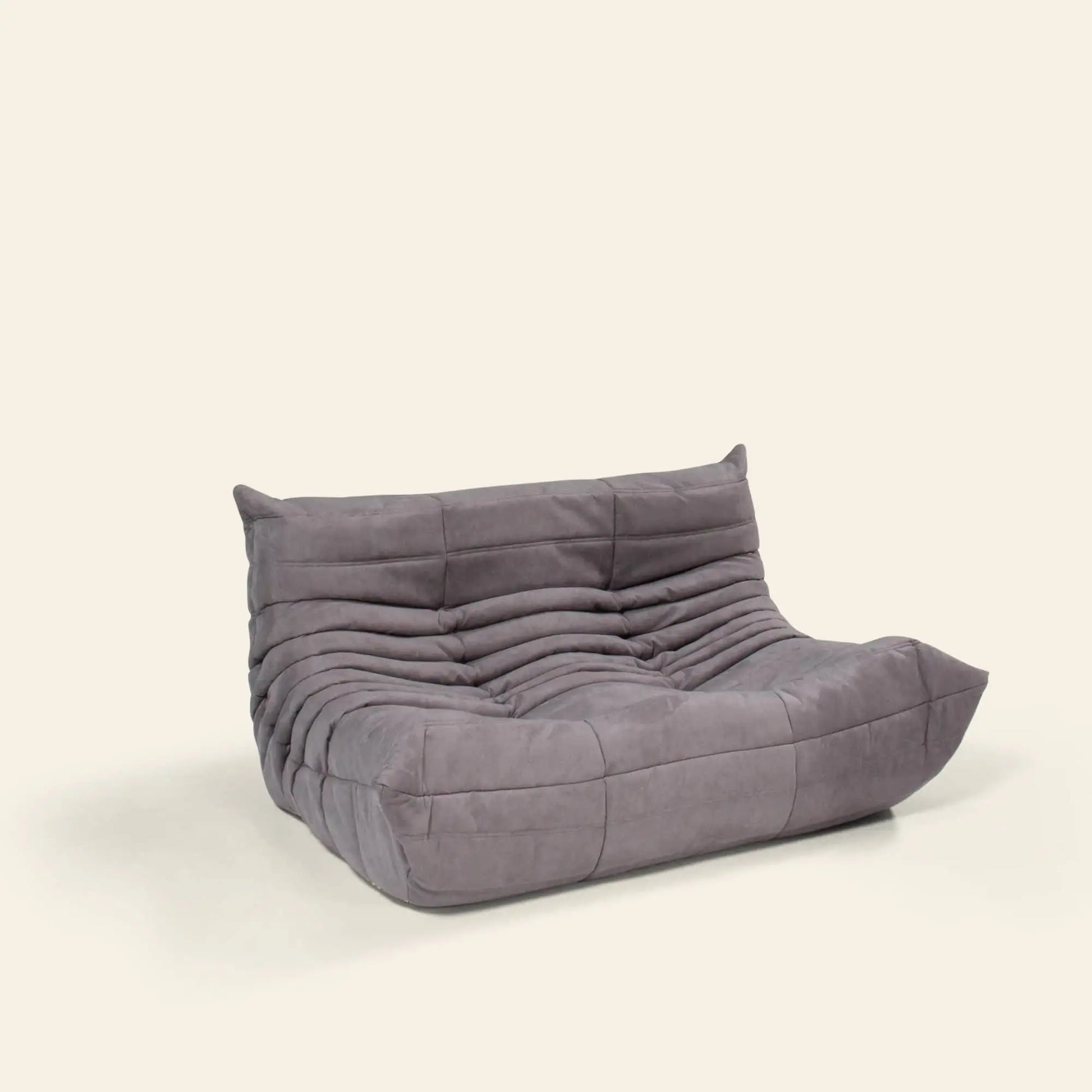 The Ligne Roset Togo, 2 Seater by Ligne Roset features a modern, low, armless design with soft gray upholstery, horizontal tufted seams, and a plush, slouched look, set against a plain light background.