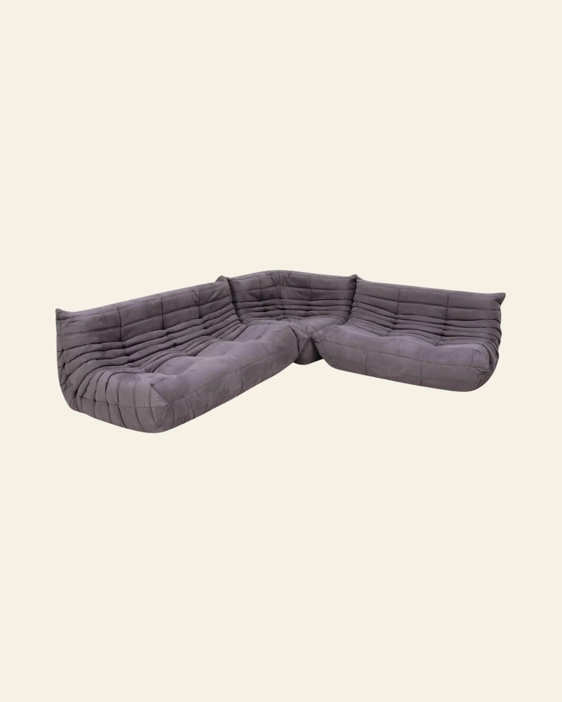 The Ligne Roset Togo, 3 Seater by Ligne Roset is a modern gray modular sofa with tufted cushions and mid-century style, set against a plain beige background.