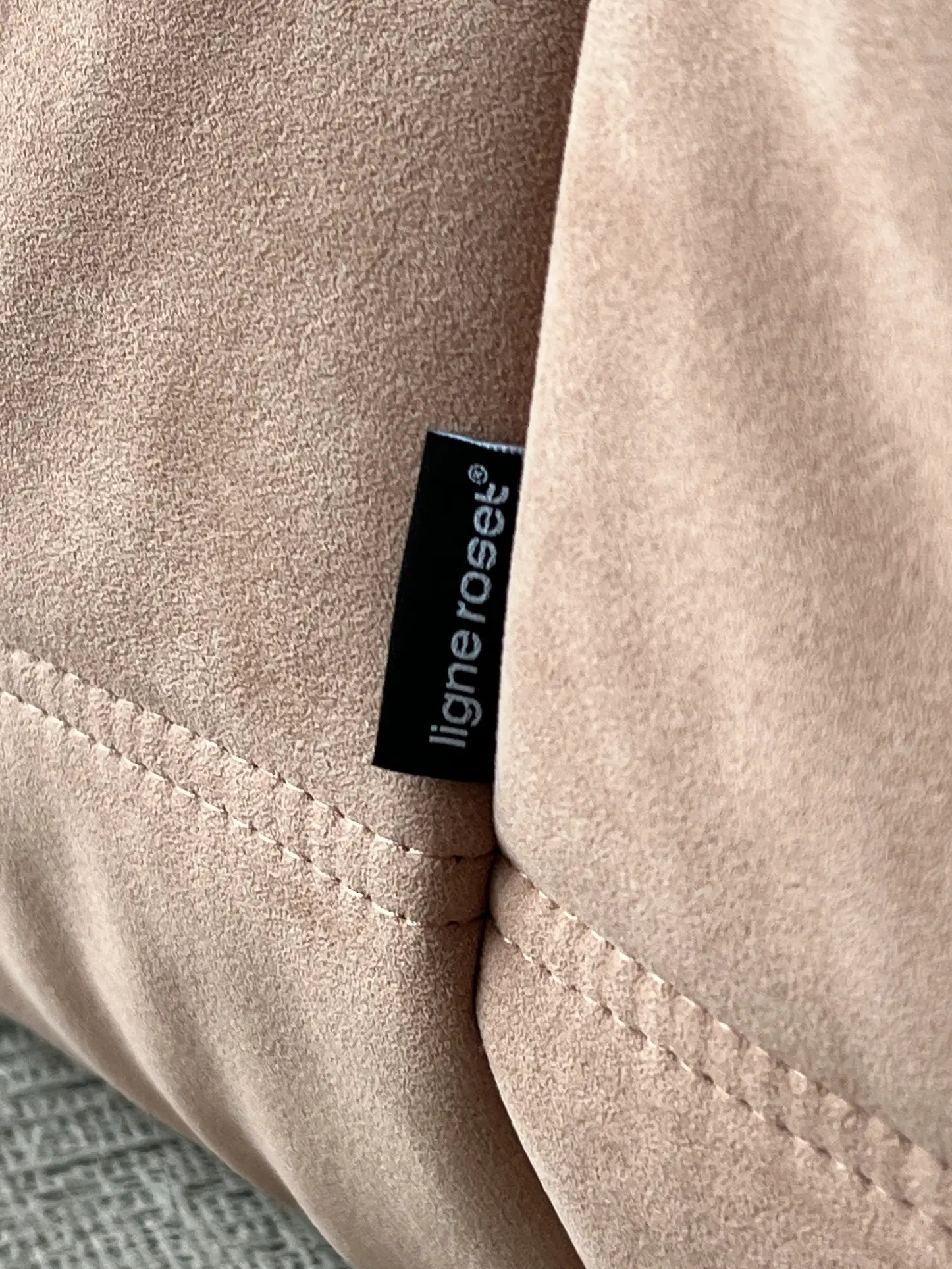 A close-up of beige suede fabric on the Ligne Roset Togo Corner Seat, showing a black fabric tag with “ligneroset” in white text and highlighting the piece’s modular design and refined craftsmanship.
