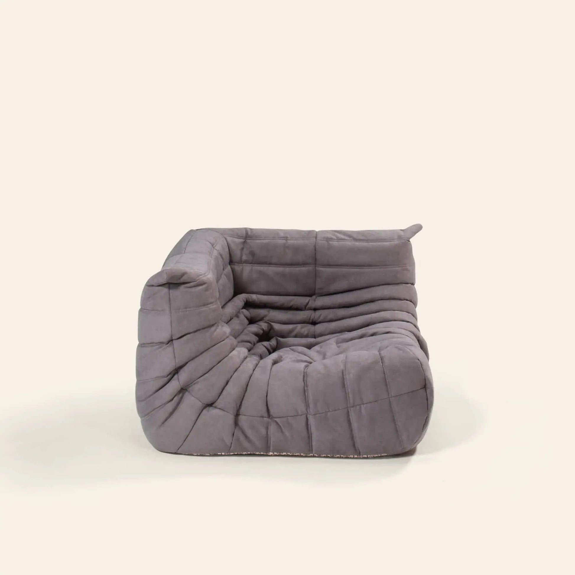 The Ligne Roset Togo Corner Seat by Ligne Roset features a modern, low-profile armless design with soft, tufted gray upholstery and a plush, segmented look, inspired by mid-century modular style.