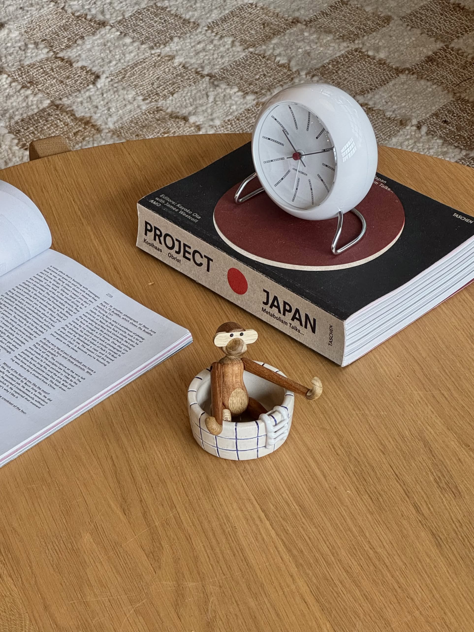 A wooden table with an open book, a Project Japan book, a white spherical clock, and a small wooden monkey figurine sitting in the handmade MIRYO Pool Ashtray by MIRYO.